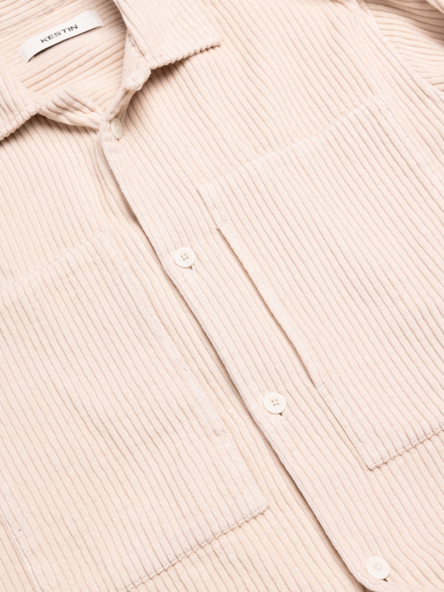 Close-up of a beige corduroy shirt with a brand label and chest pockets