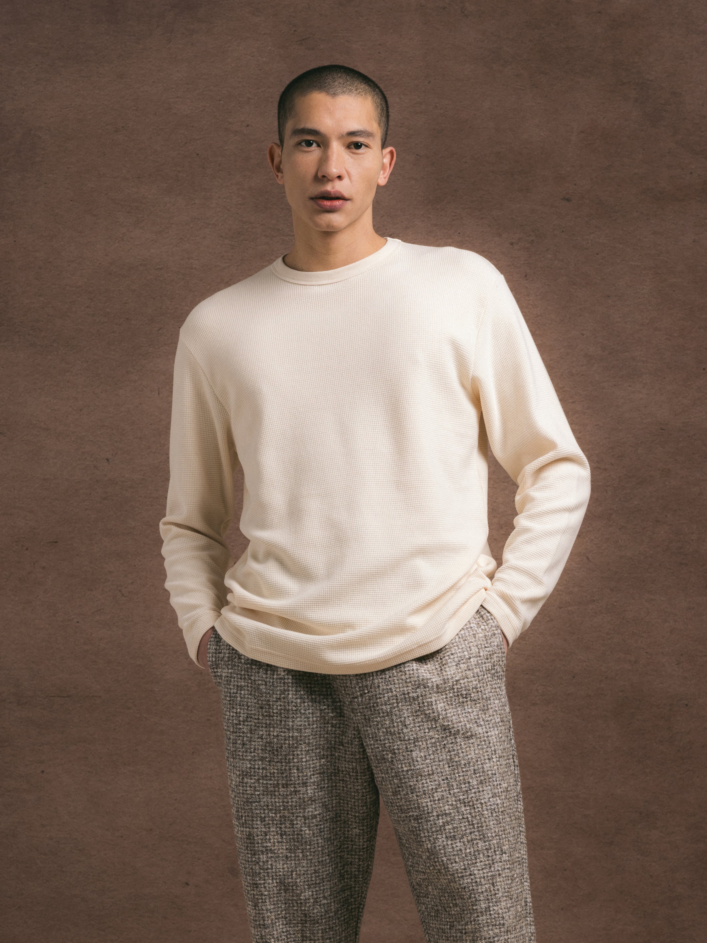 A man wearing a waffle texture, nautral colour cotton long sleeve tee  and gray trousers