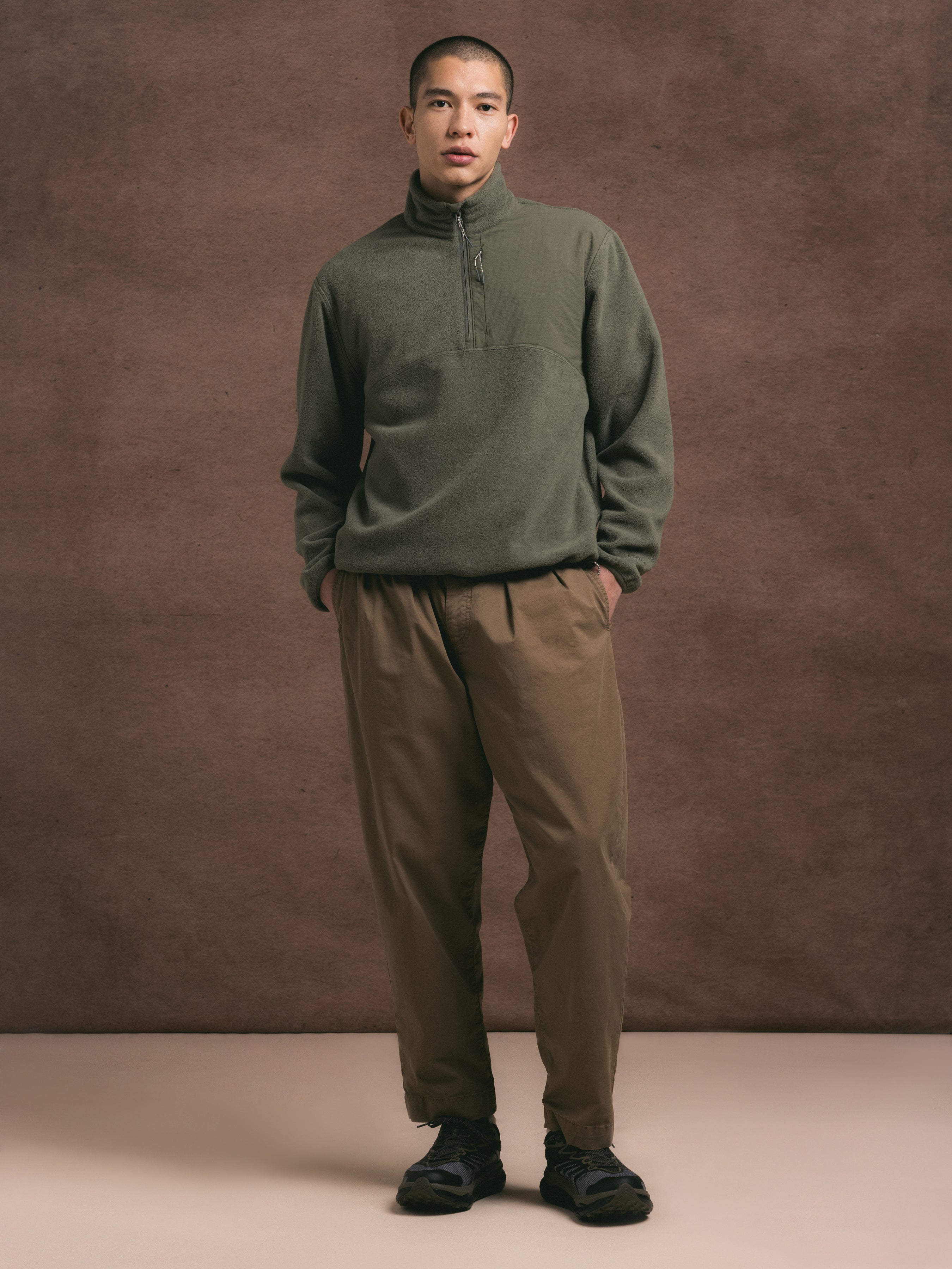 man wearing a green pullover fleece against a brown background.