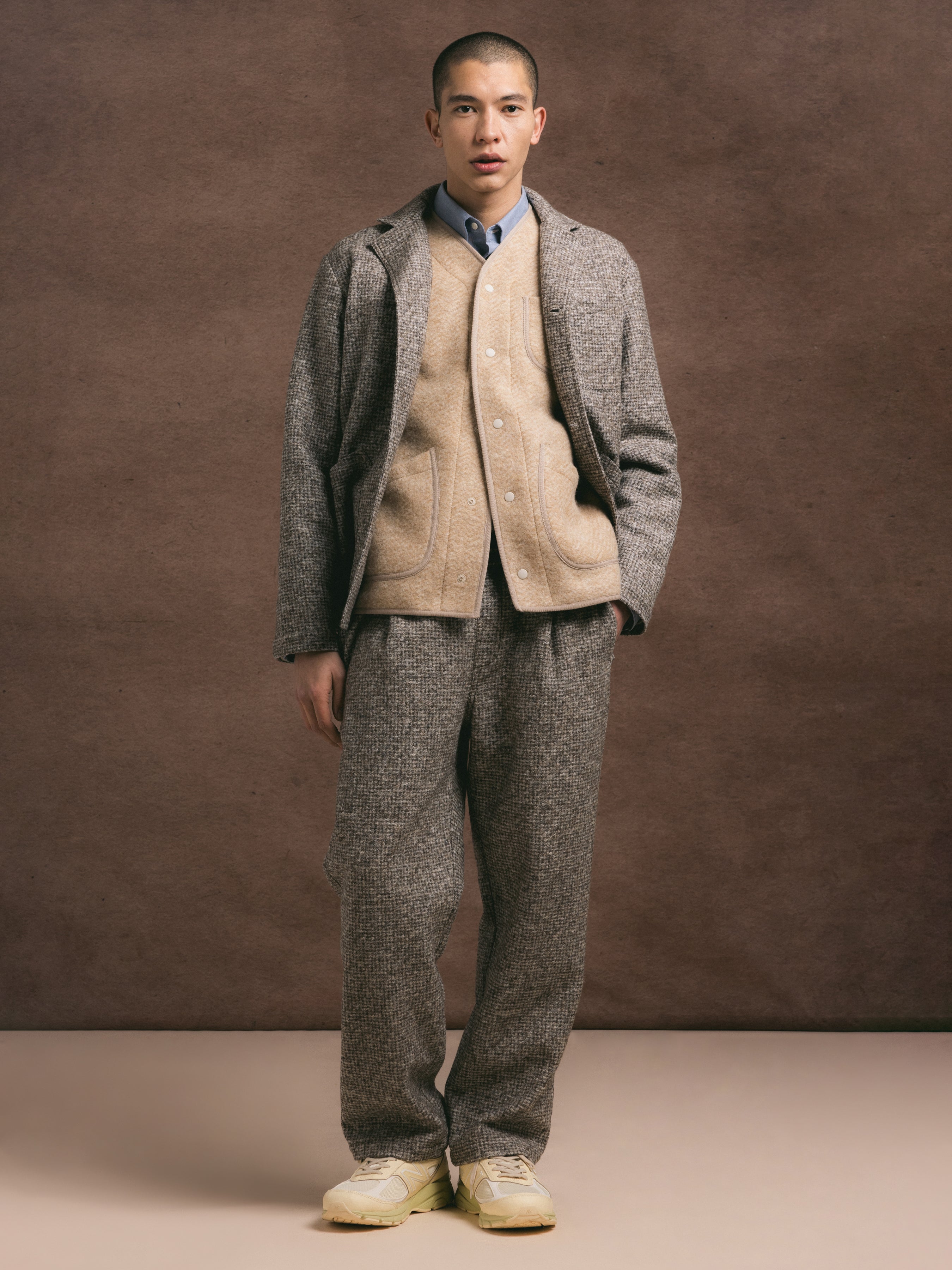 A man wearing a layered outfit with a wool blend two piece suit paired with an oat cardigan