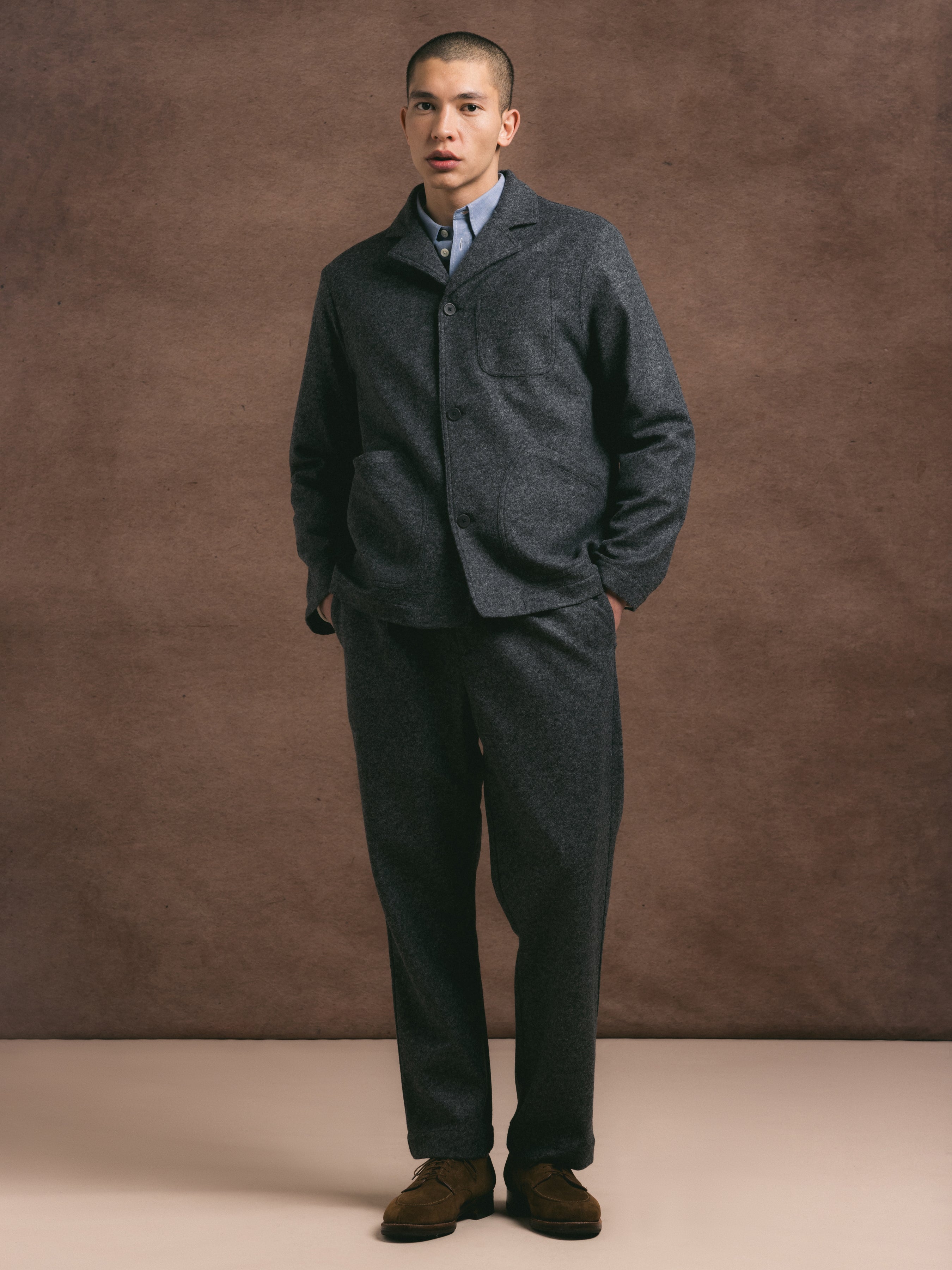 A man wearing a charcoal two piece premium wool blend suit against a brown background