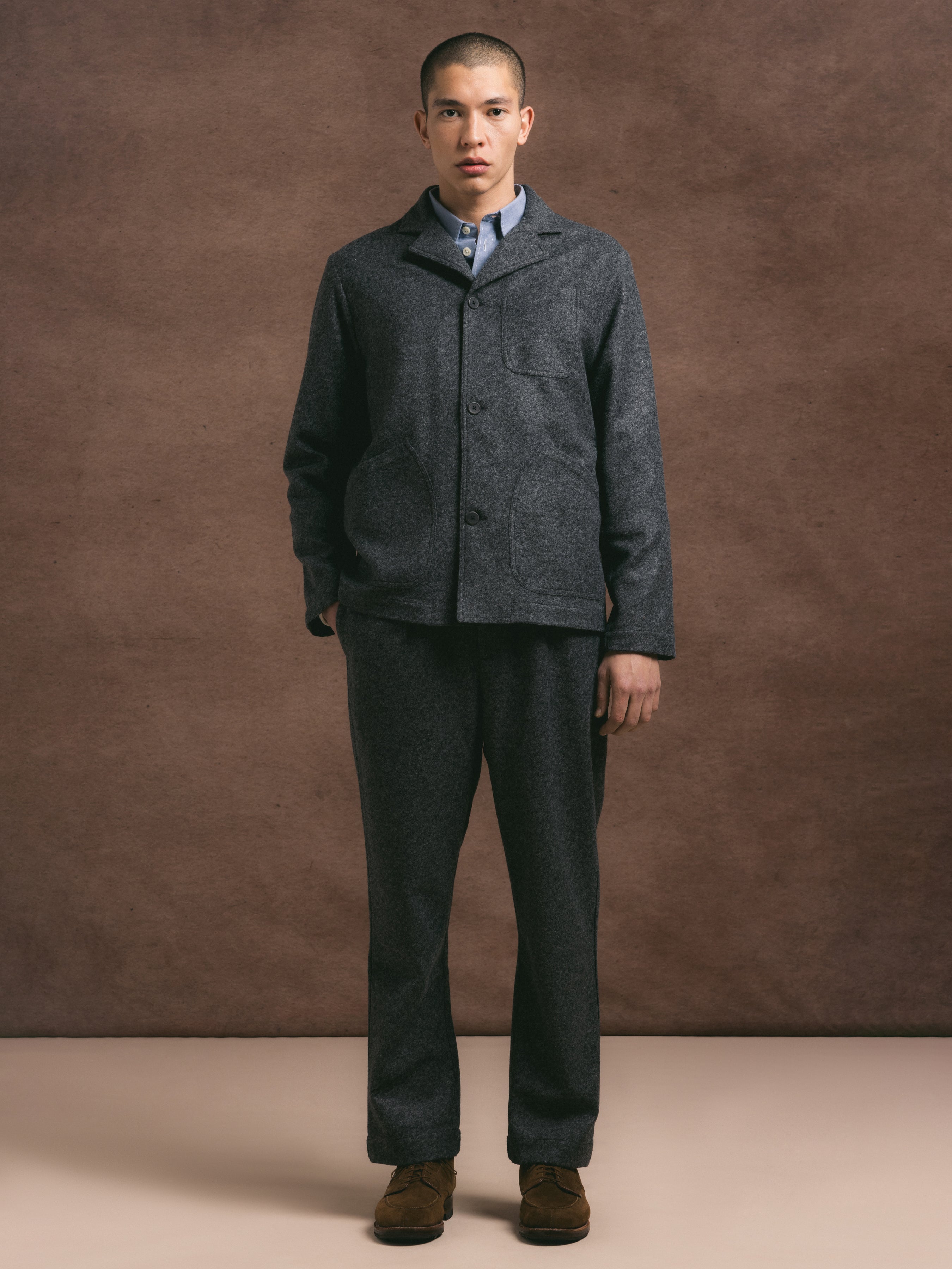 A model wearing a two piece suit in a charcoal wool blend fabric against a brown background