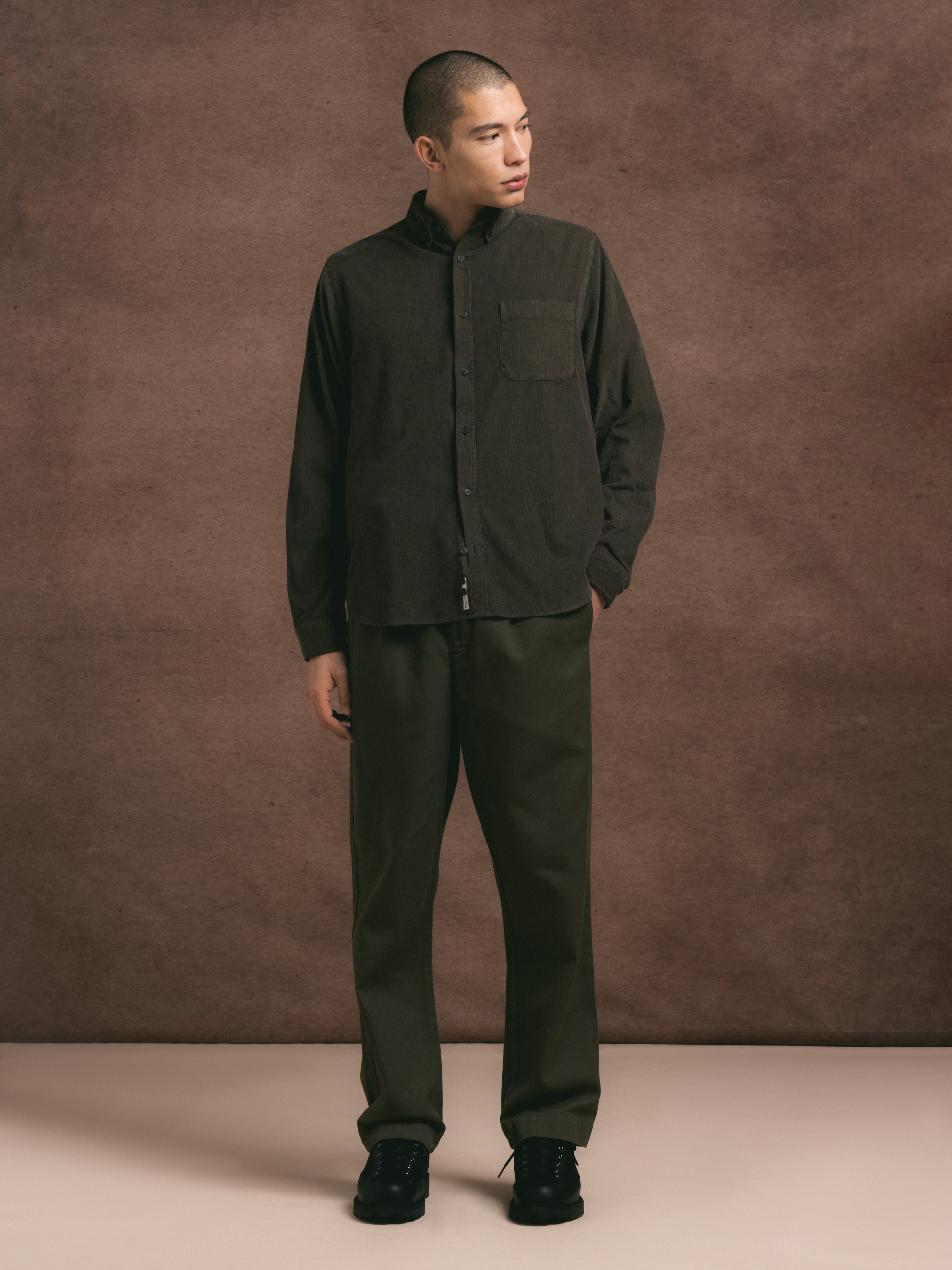 A model wearing a two piece regular fit suit in dark olive cotton twill against a brown background