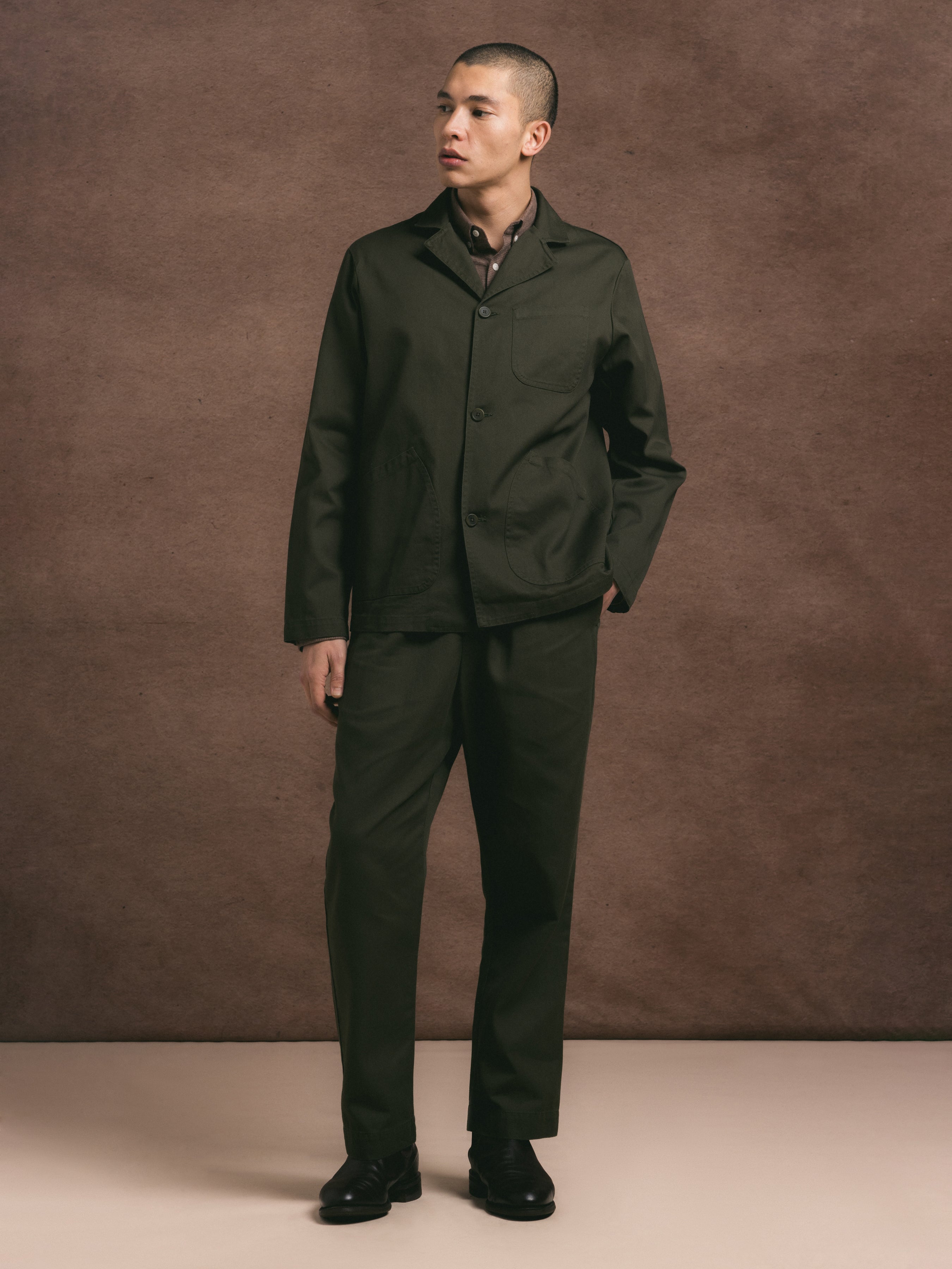 A model wearing a two piece regular fit suit in dark olive cotton twill with a brown shirt underneath