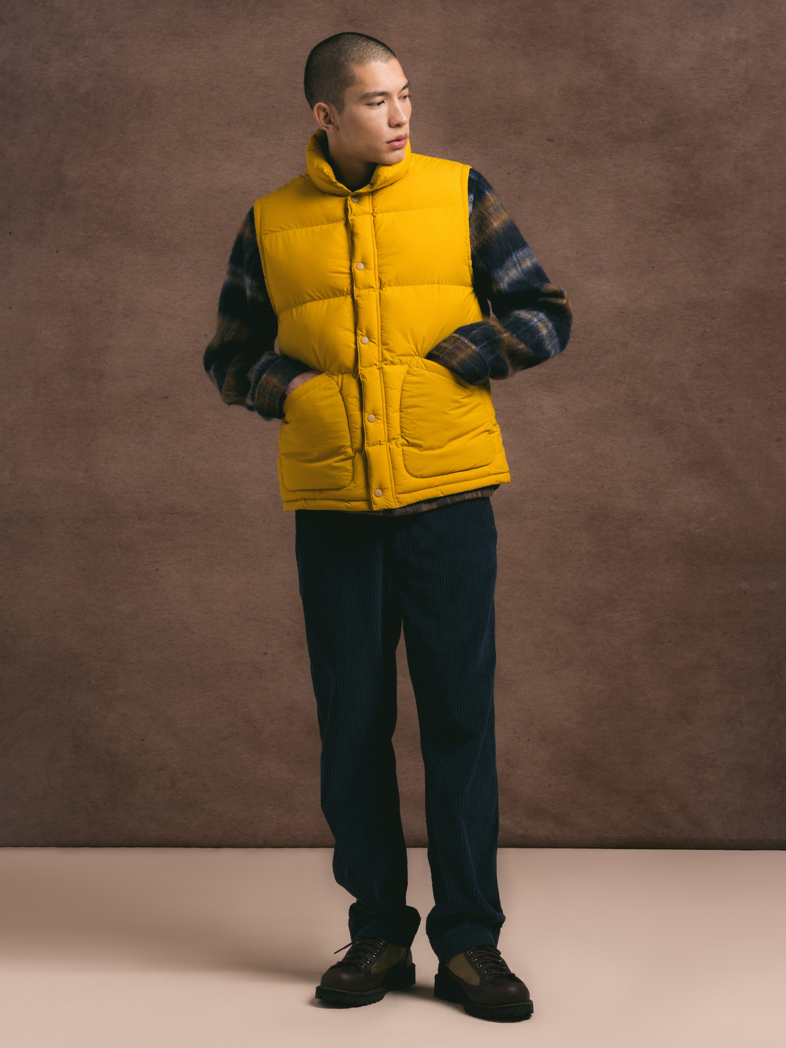 Person wearing a yellow puffer vest over a patterned jacket against a brown background