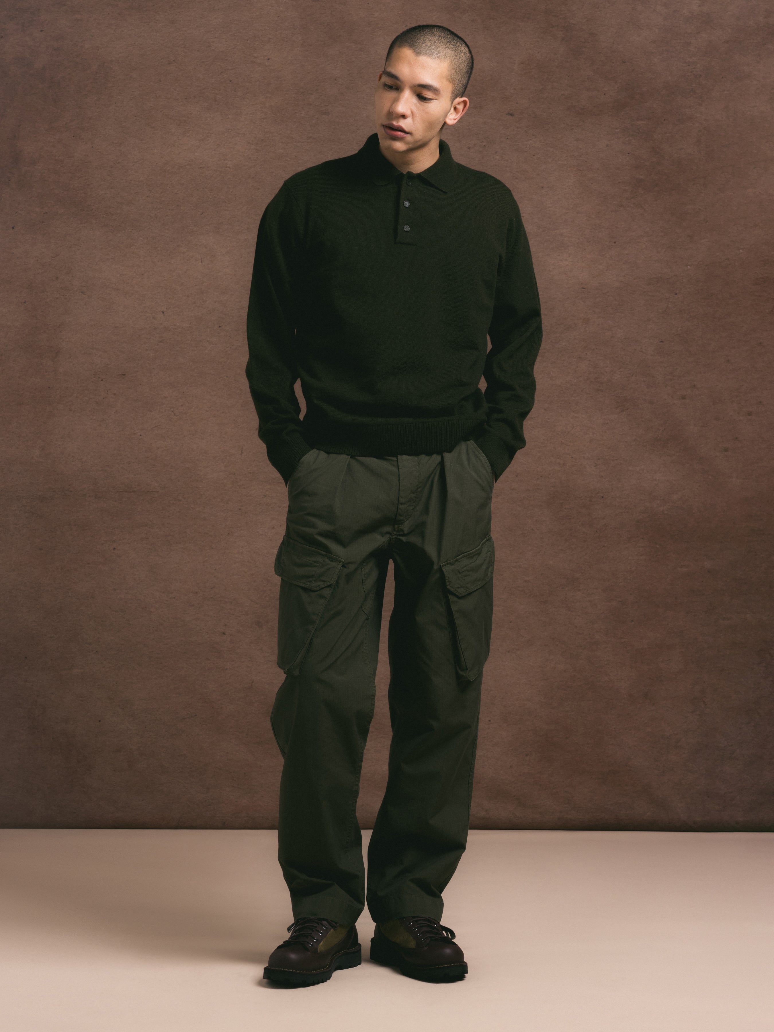 Man wearing a dark green sweater and pants against a brown background