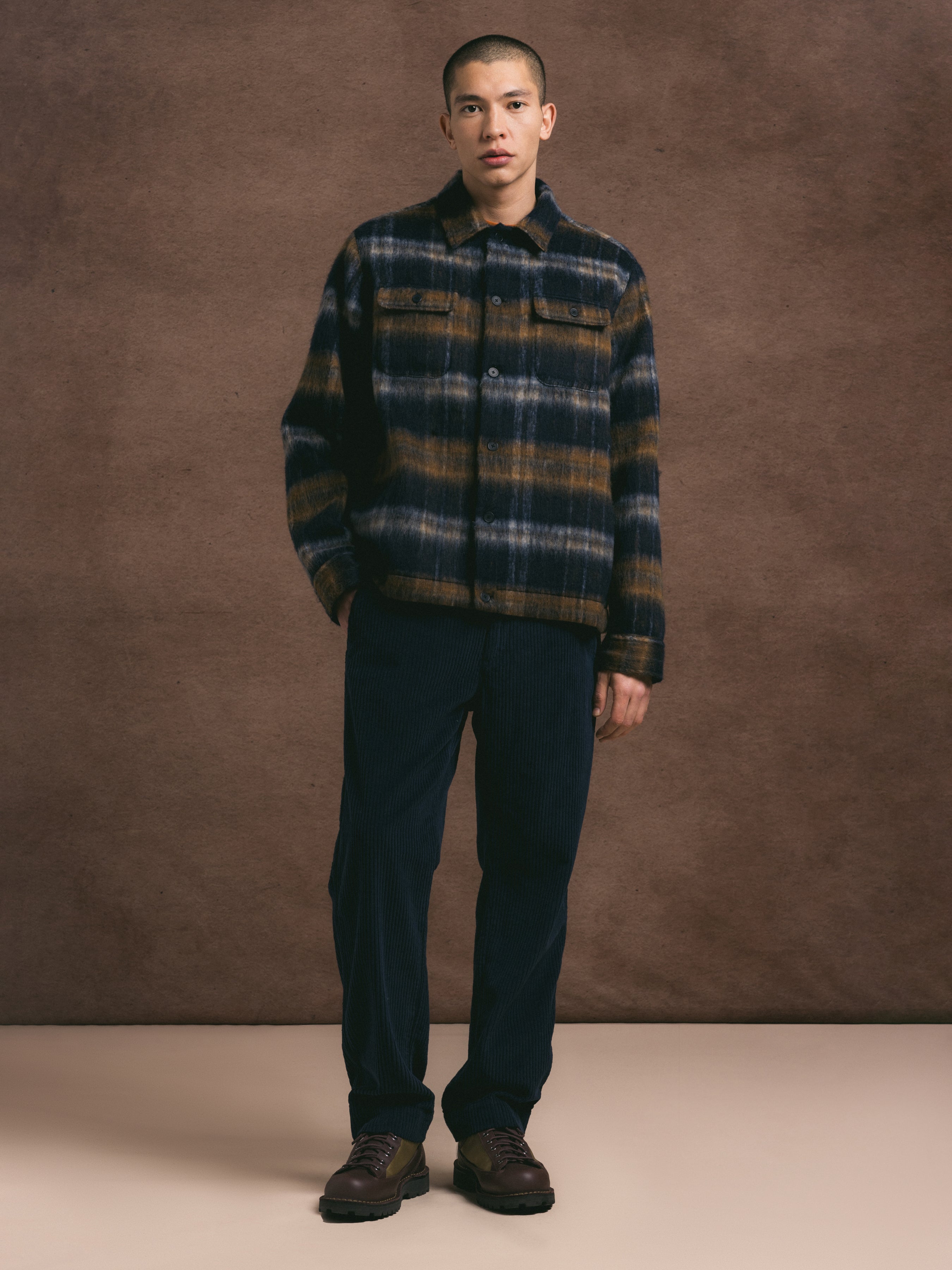 Man wearing a plaid wool jacket and navy blue trousers against a brown background