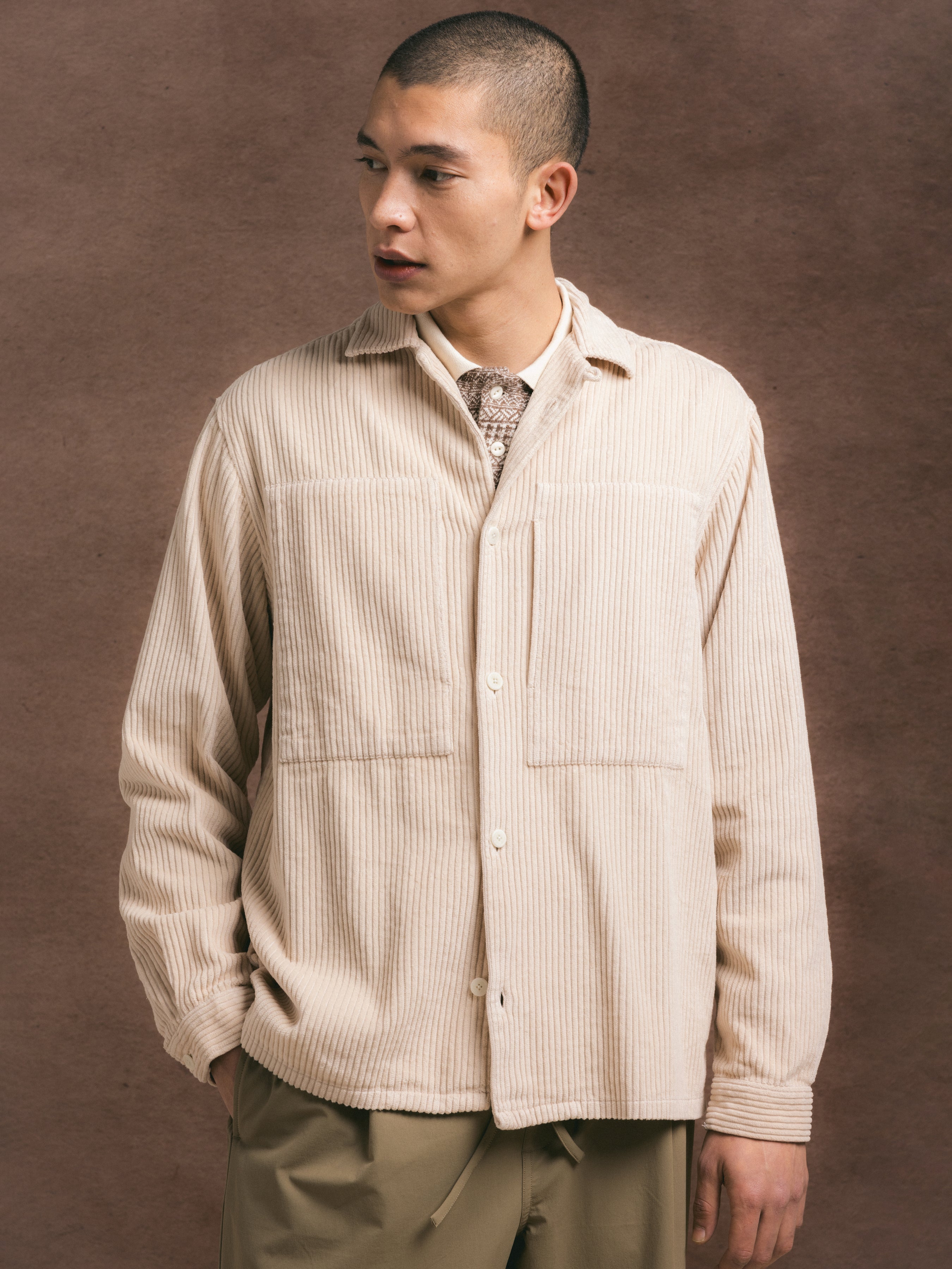 Man wearing a beige corduroy overshirt against a brown background