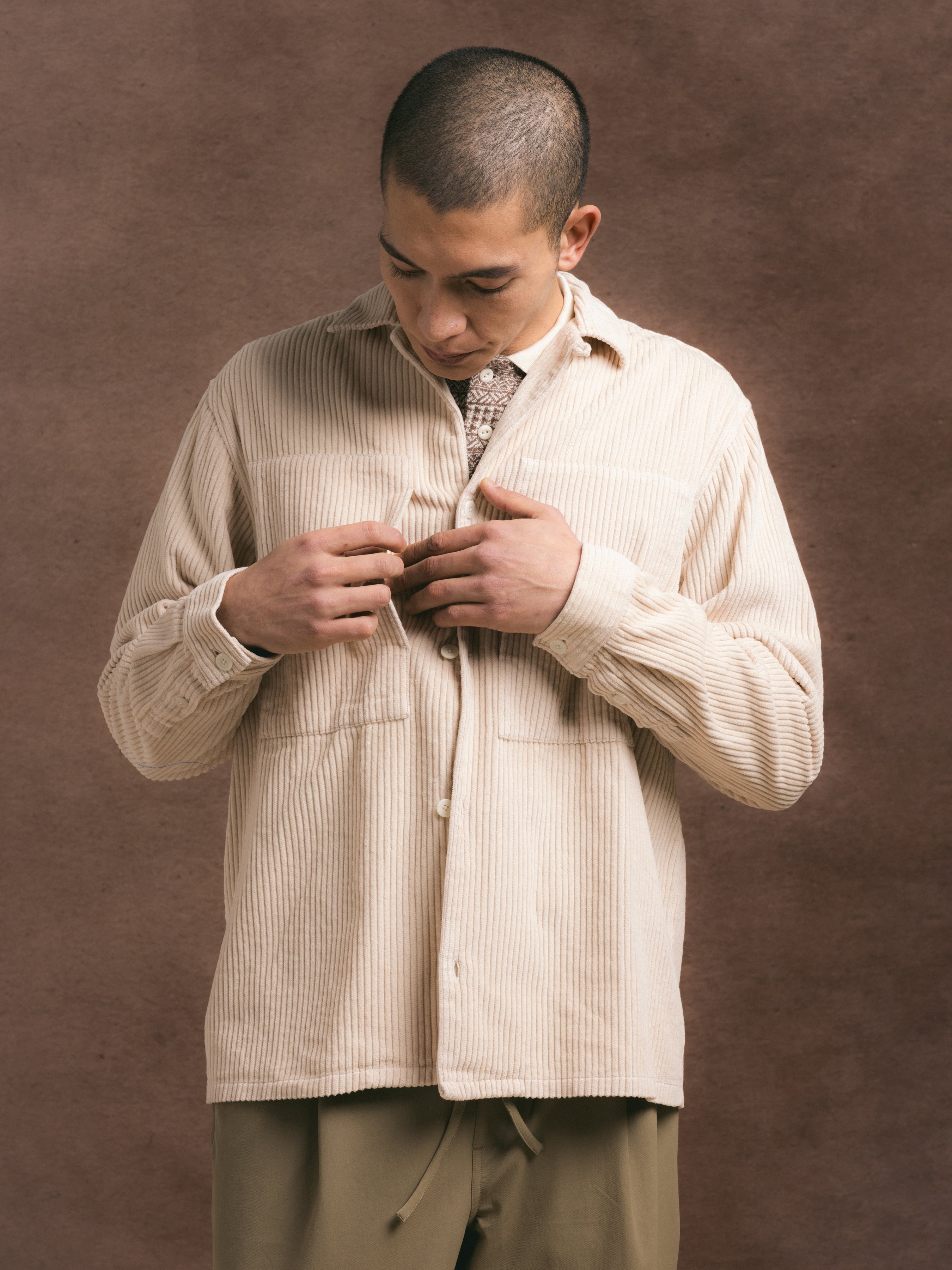 A model showing a corduroy overshirt from KESTIN, against a brown background