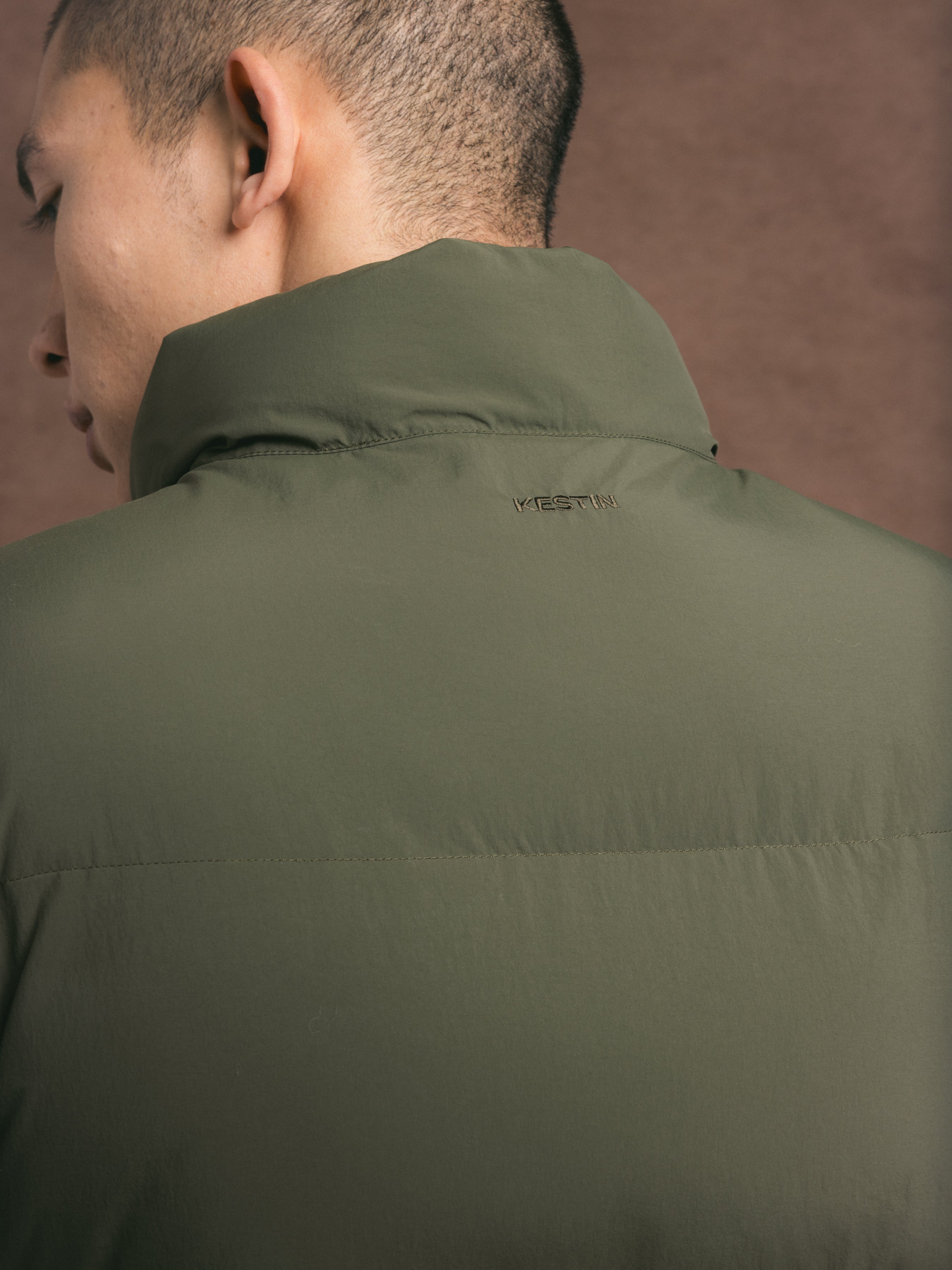 Person wearing a green jacket with a KESTIN logo on a brown background