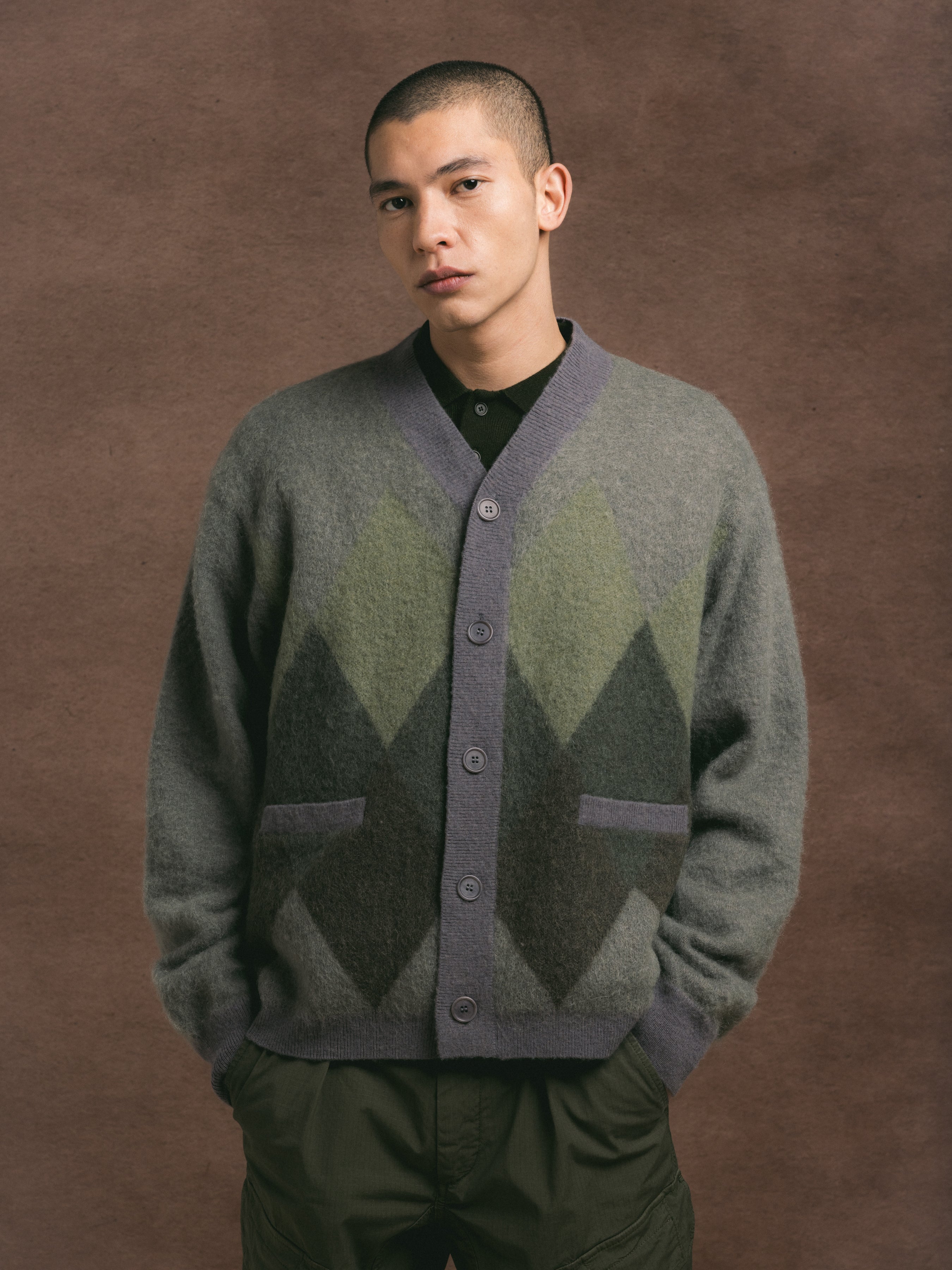Man wearing a patterned cardigan against a brown background