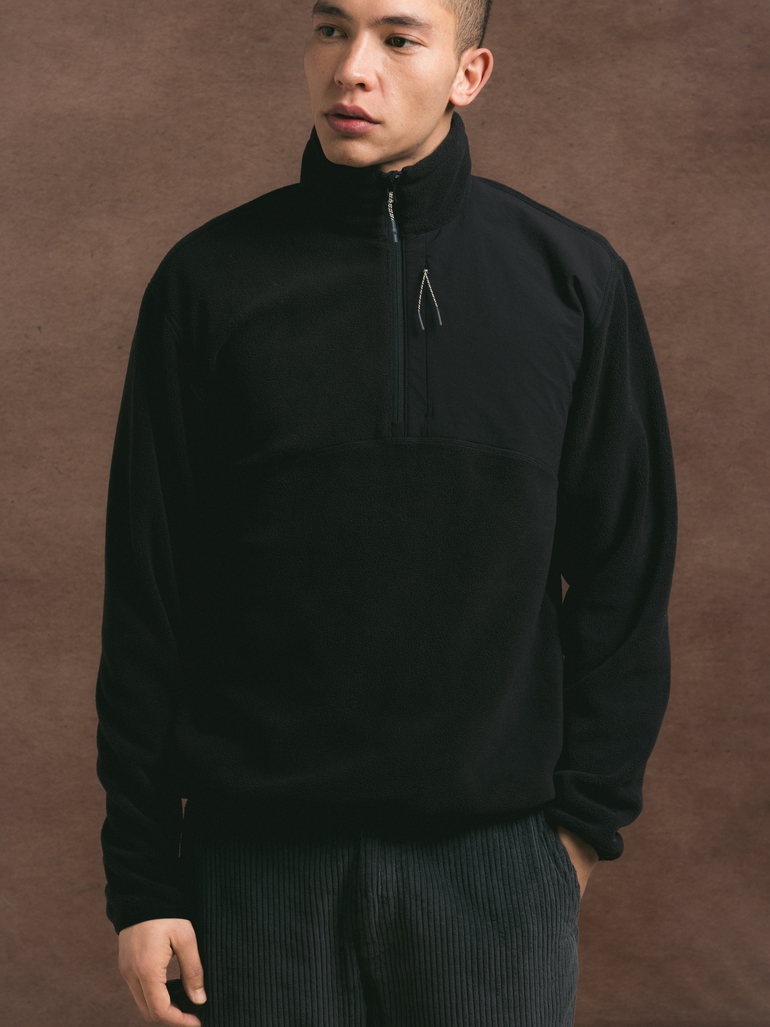 Person wearing a black quarter-zip fleece against a brown background