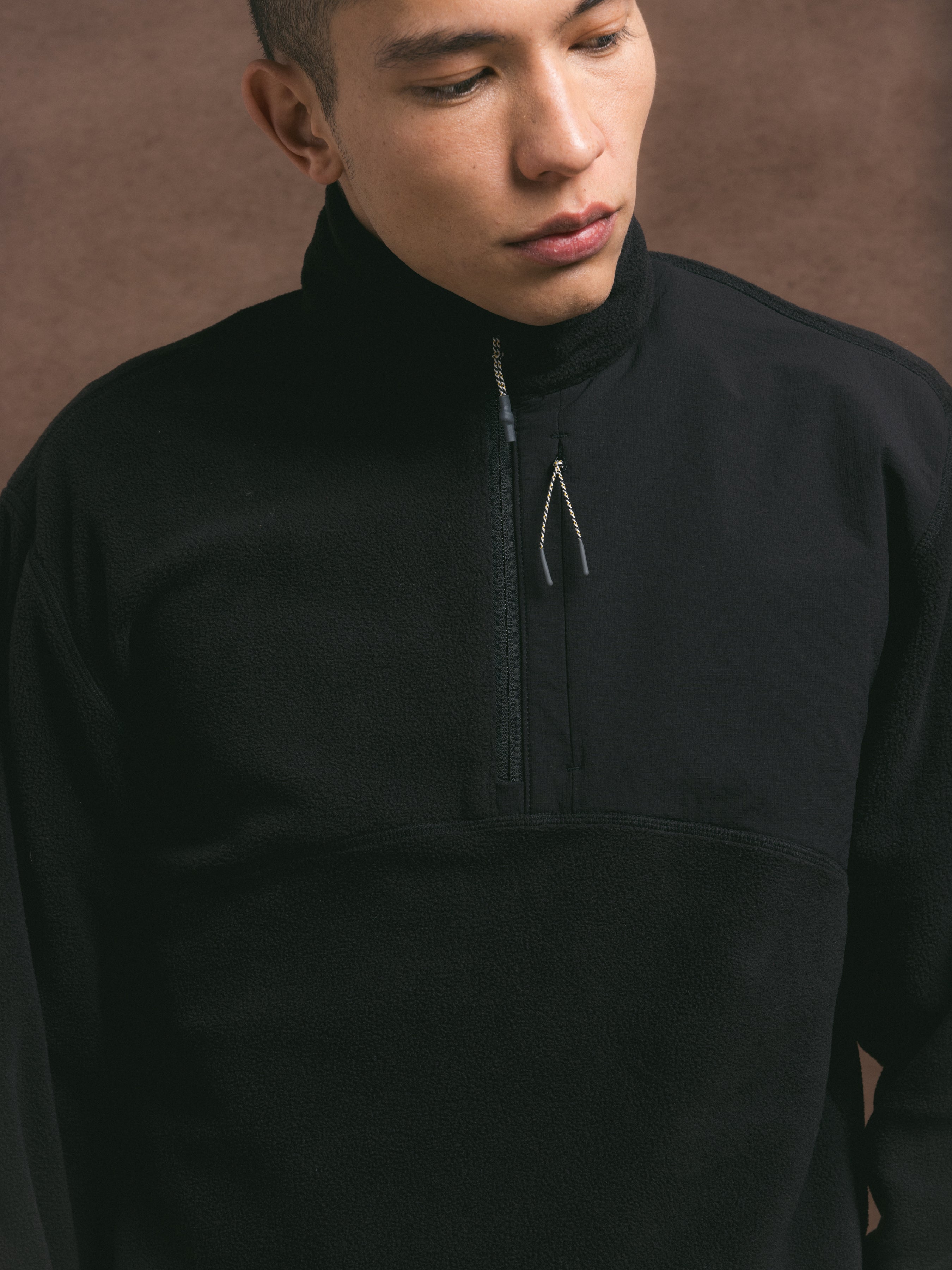 Person wearing a black quarter-zip fleece against a brown background