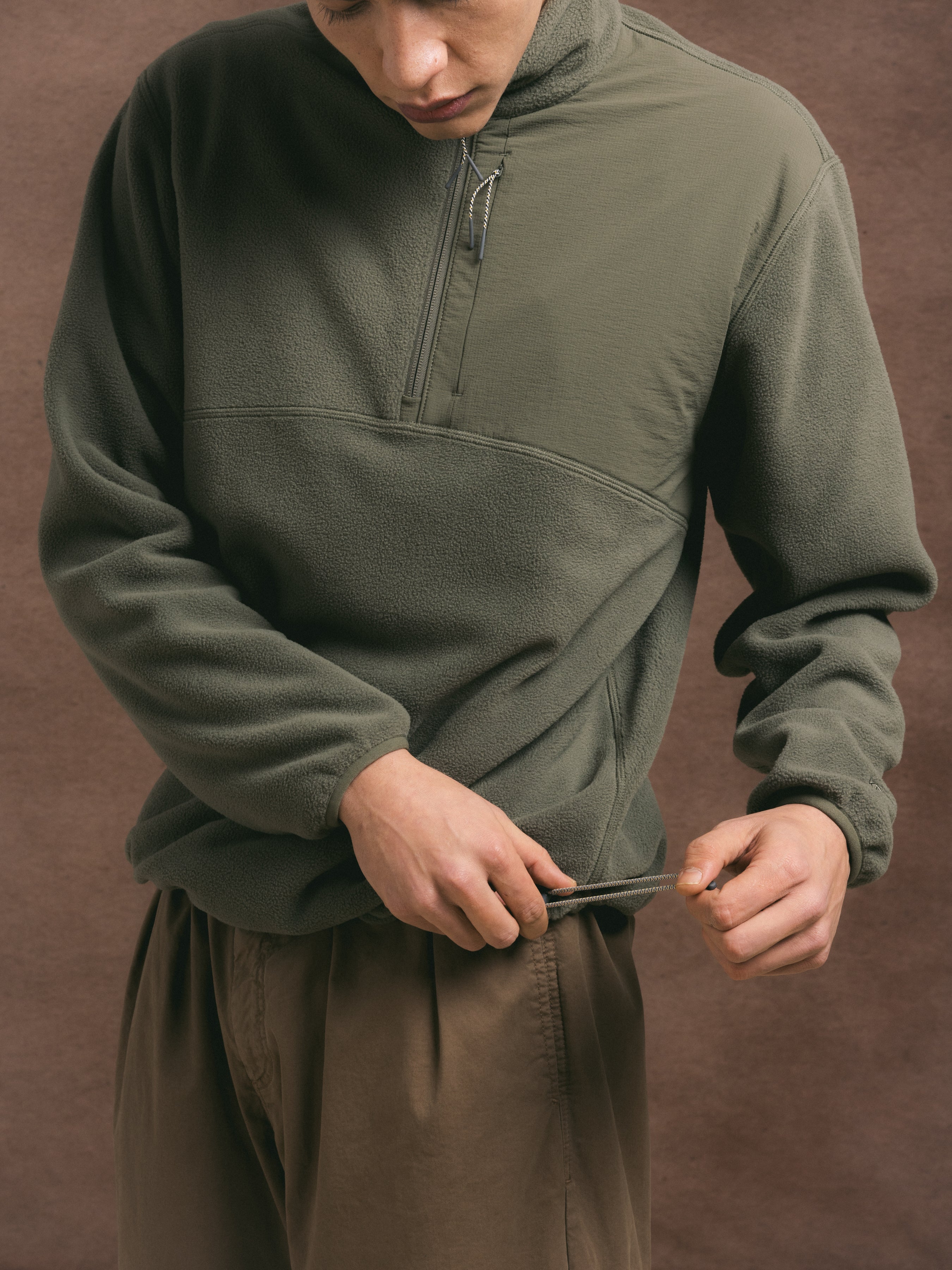 A man synching the hem of the KESTIN Aberfeldy Fleece in green.