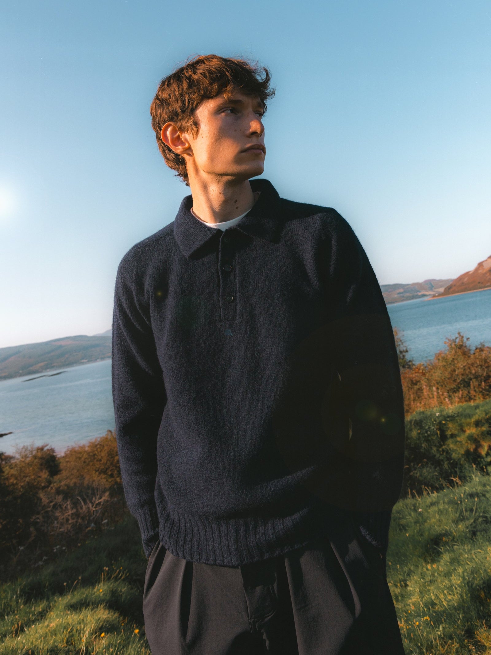 A model wearing a navy blue knitted polo, made in Scotland.