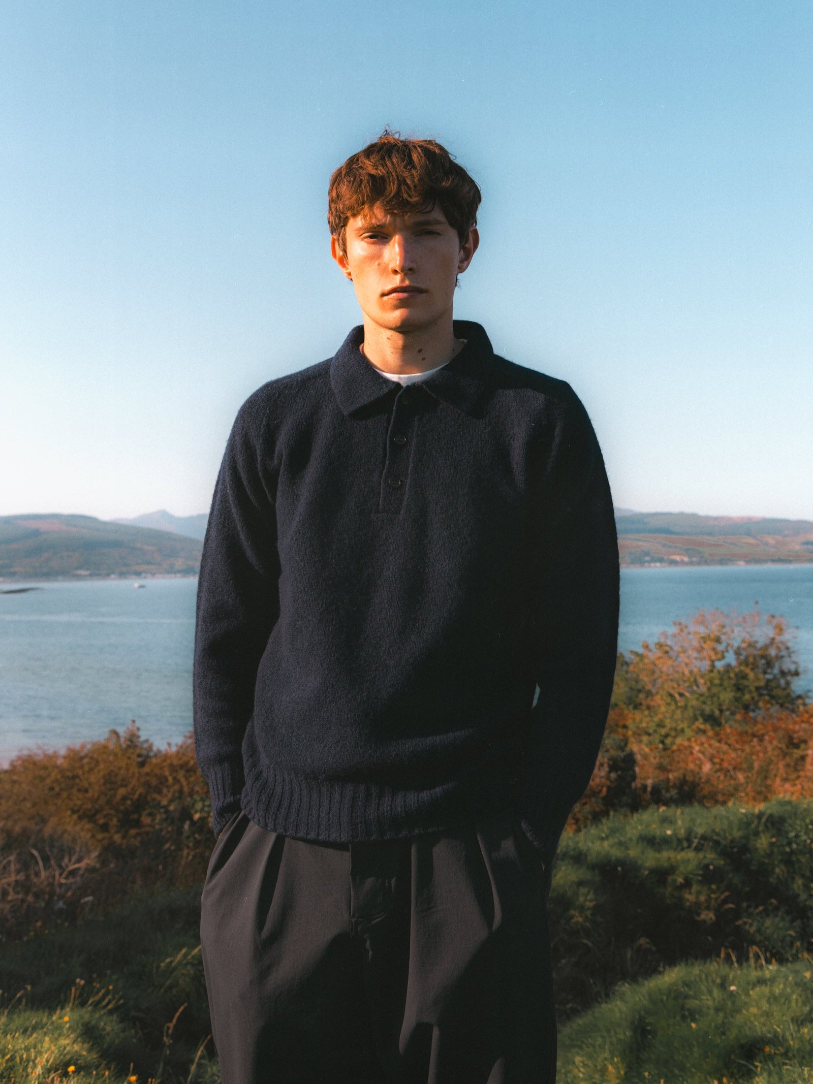 A man wearing a knitted polo sweater in navy blue, made in Scotland.