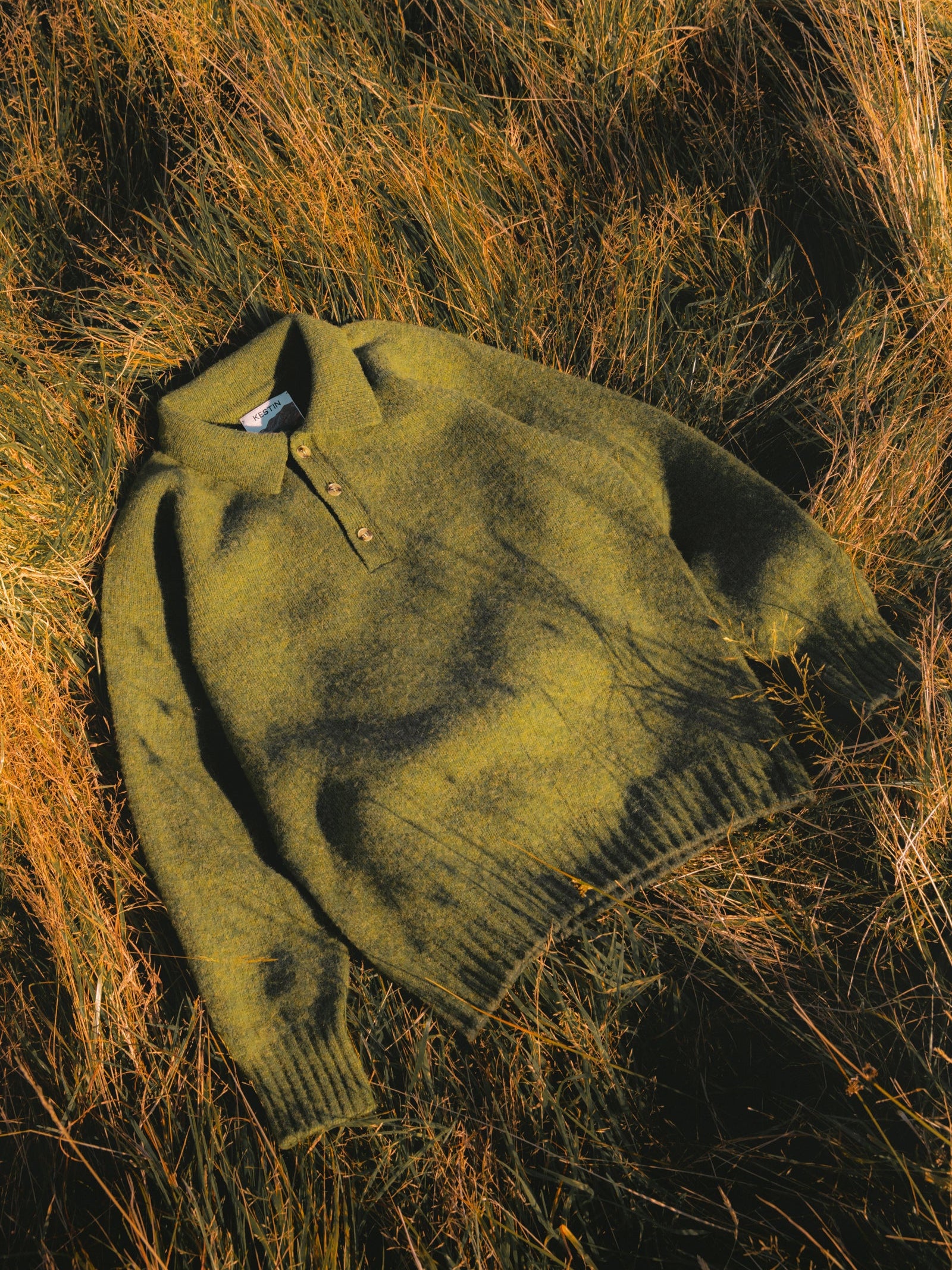 A green shetland wool polo shirt, pictured in some grass on the Isle of Arran.