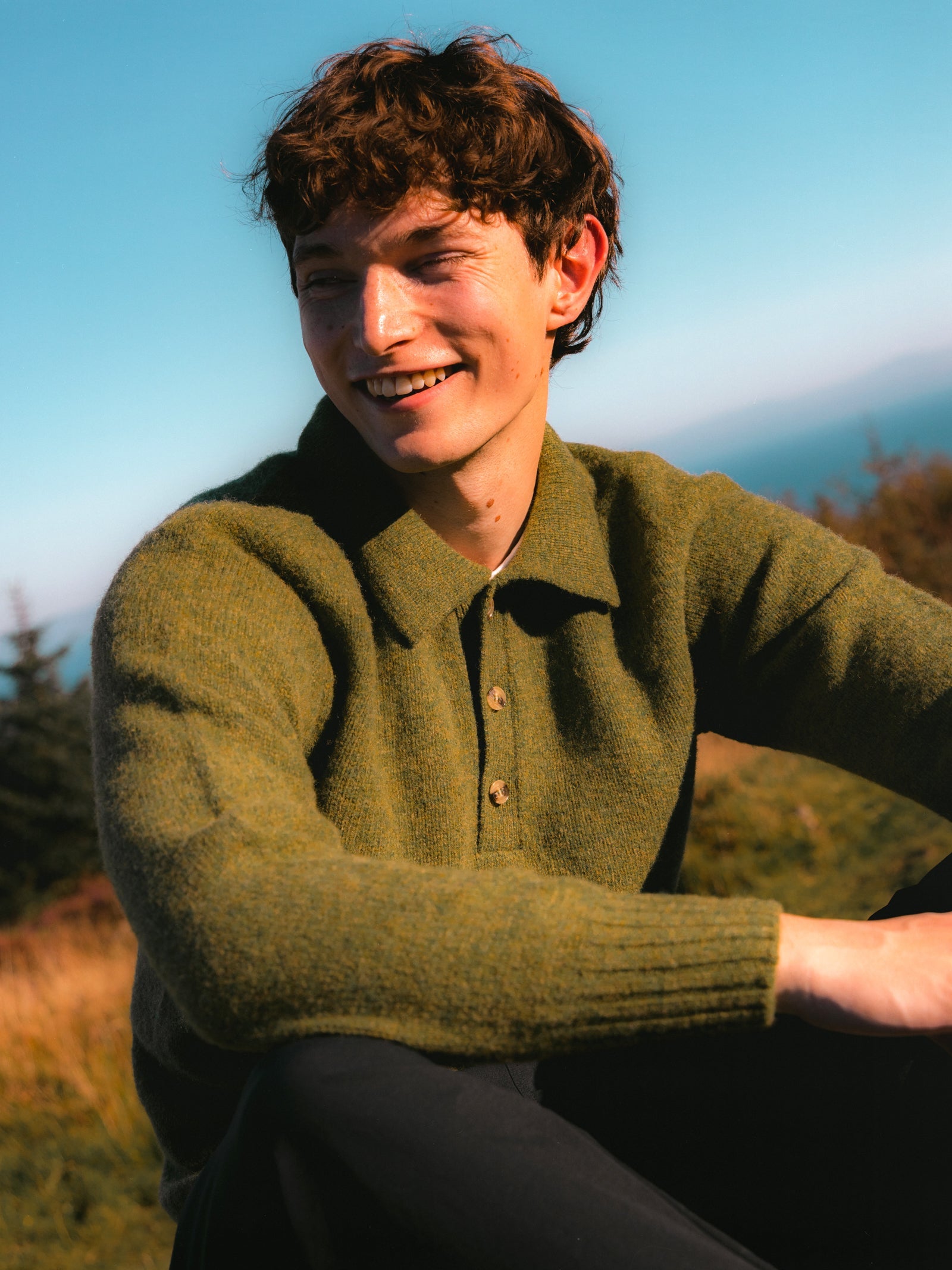 A model wearing a green knitted polo sweater, on the Isle of Arran.