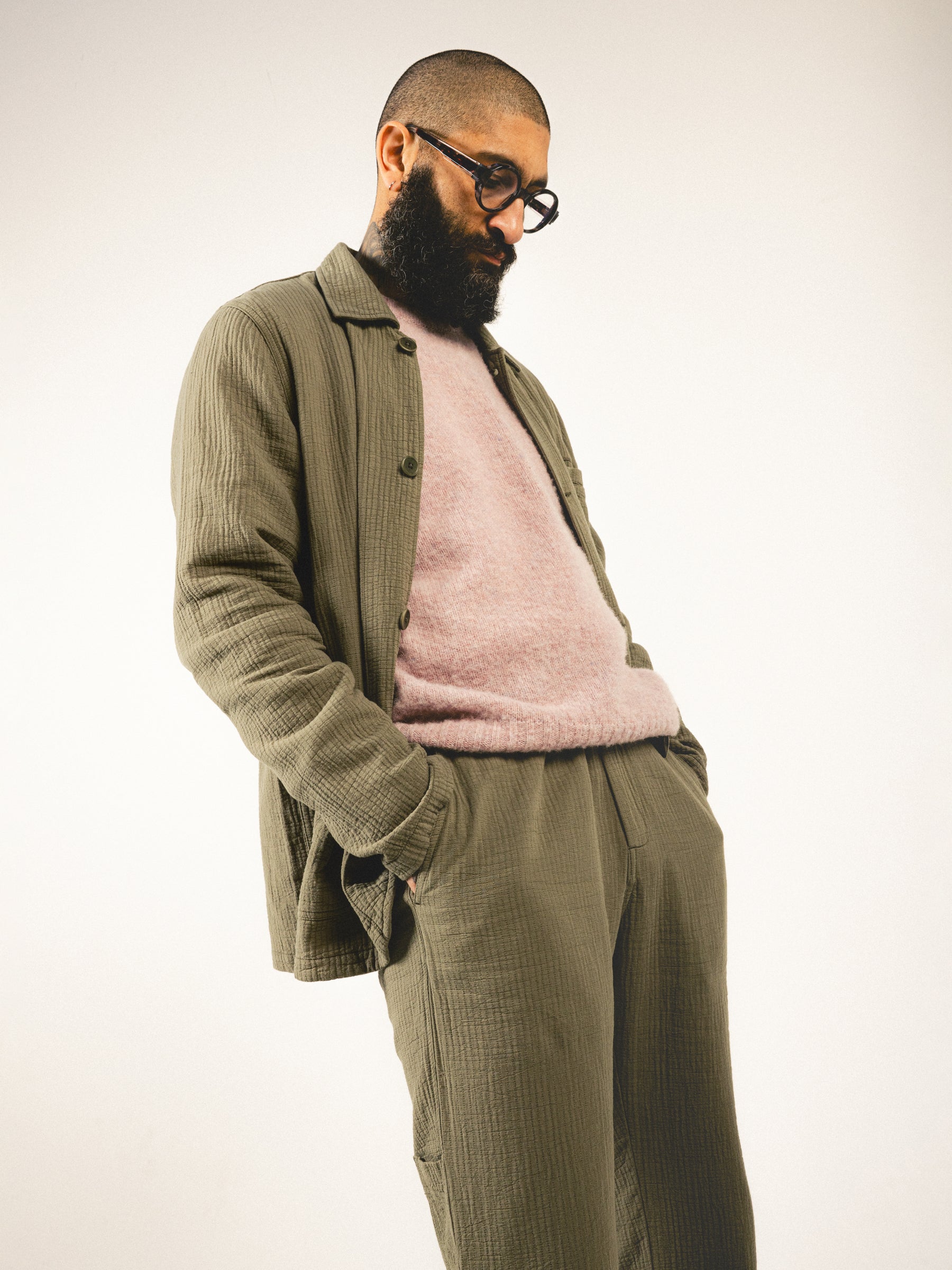 A man wearing a pink knitted sweater underneath an olive green suit.