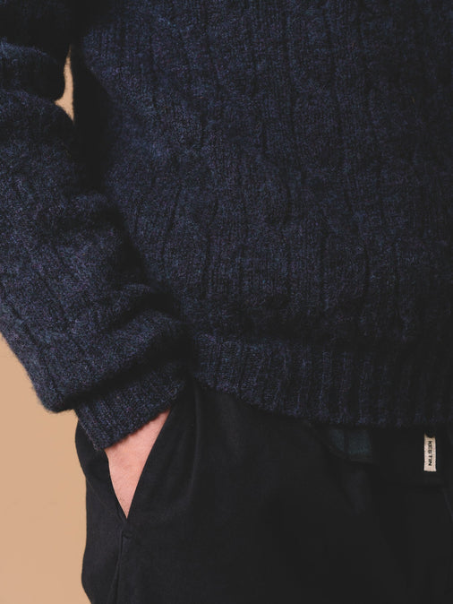 The ribbed hem and cuff of a cable knit sweater, with the man's hand in his pocket.