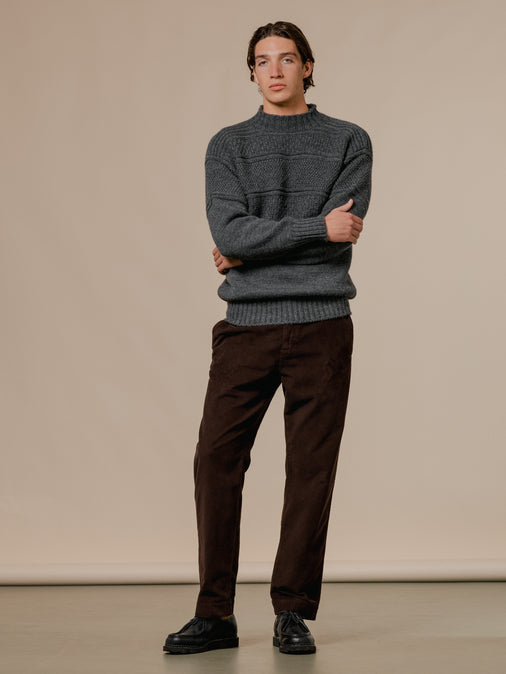 A model wearing a knitted sweater in charcoal grey, made in Scotland.