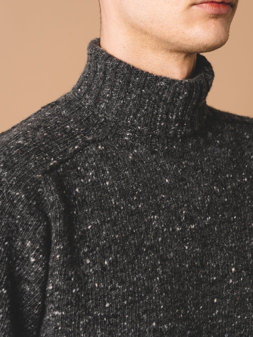 A man wearing a knitted roll neck sweater, made in Scotland from Donegal wool.