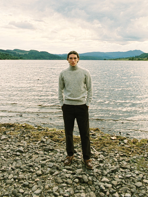 A man wearing a knitted roll neck sweater, stood on a beach on the Isle of Skye.