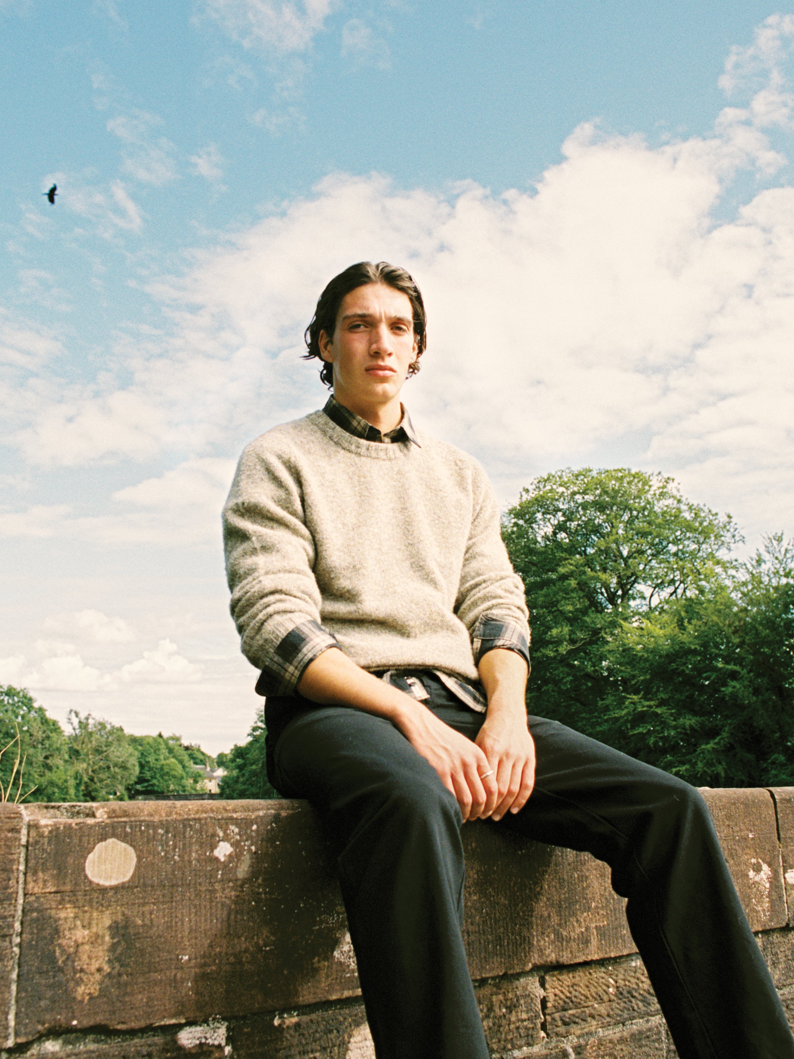 A man sitting on a wall in the Isle of Skye, wearing a Shetland wool sweater.