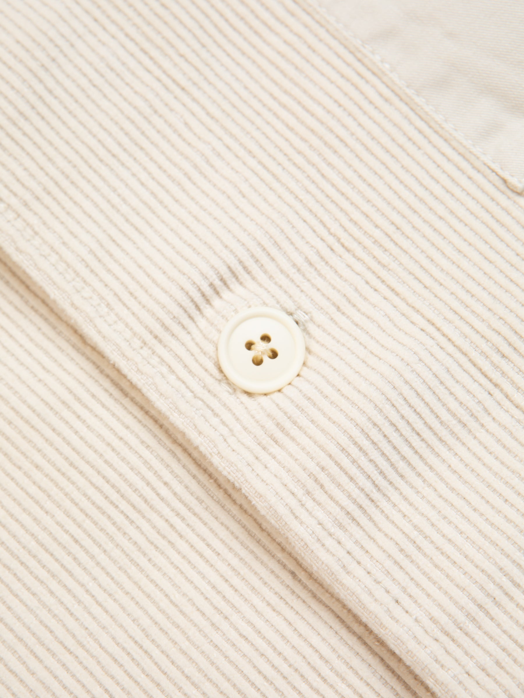 A button on the front of a men's corduroy overshirt.