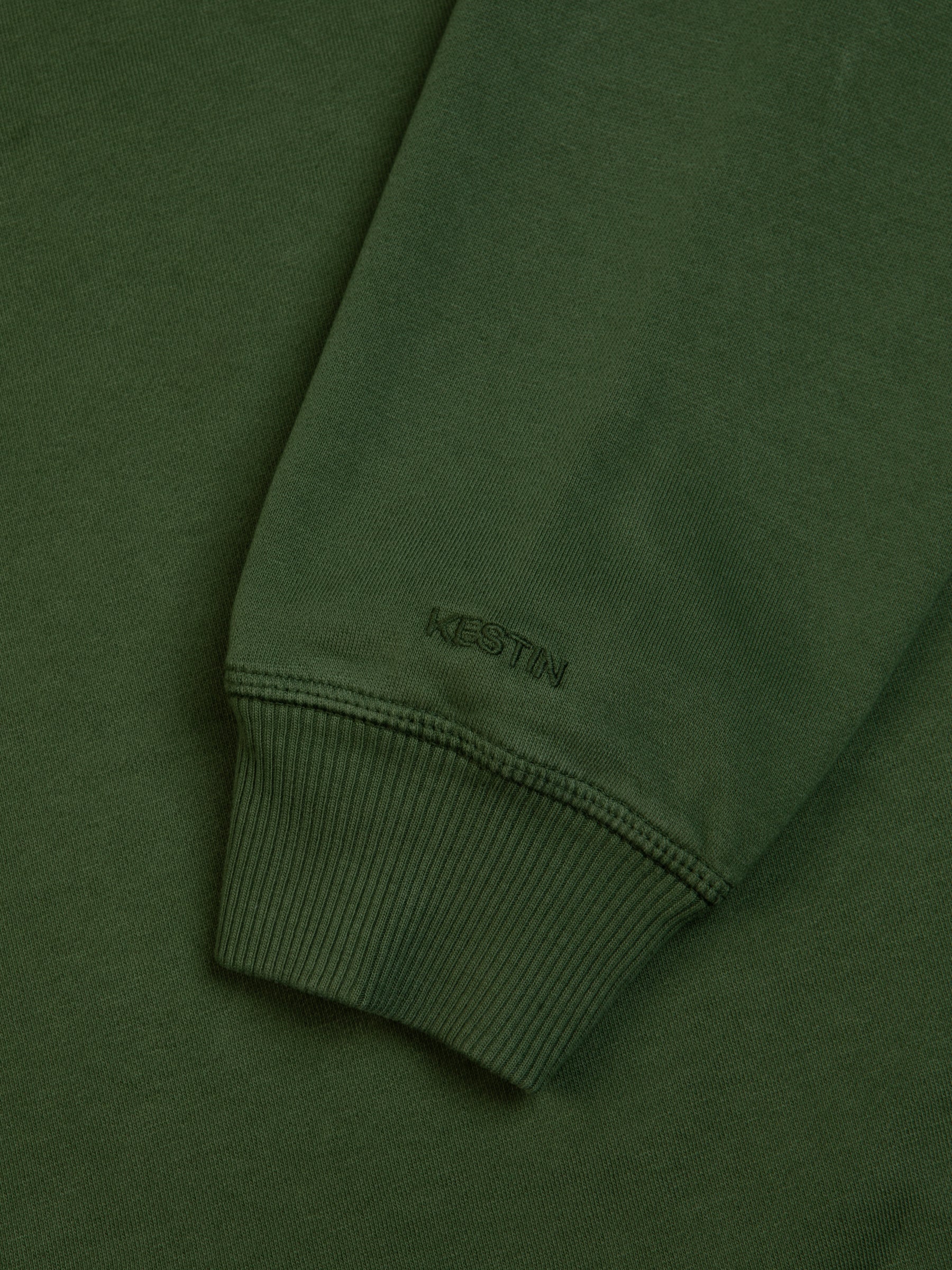A garment dyed green sweatshirt with a logo embroidered to the ribbed cuff.