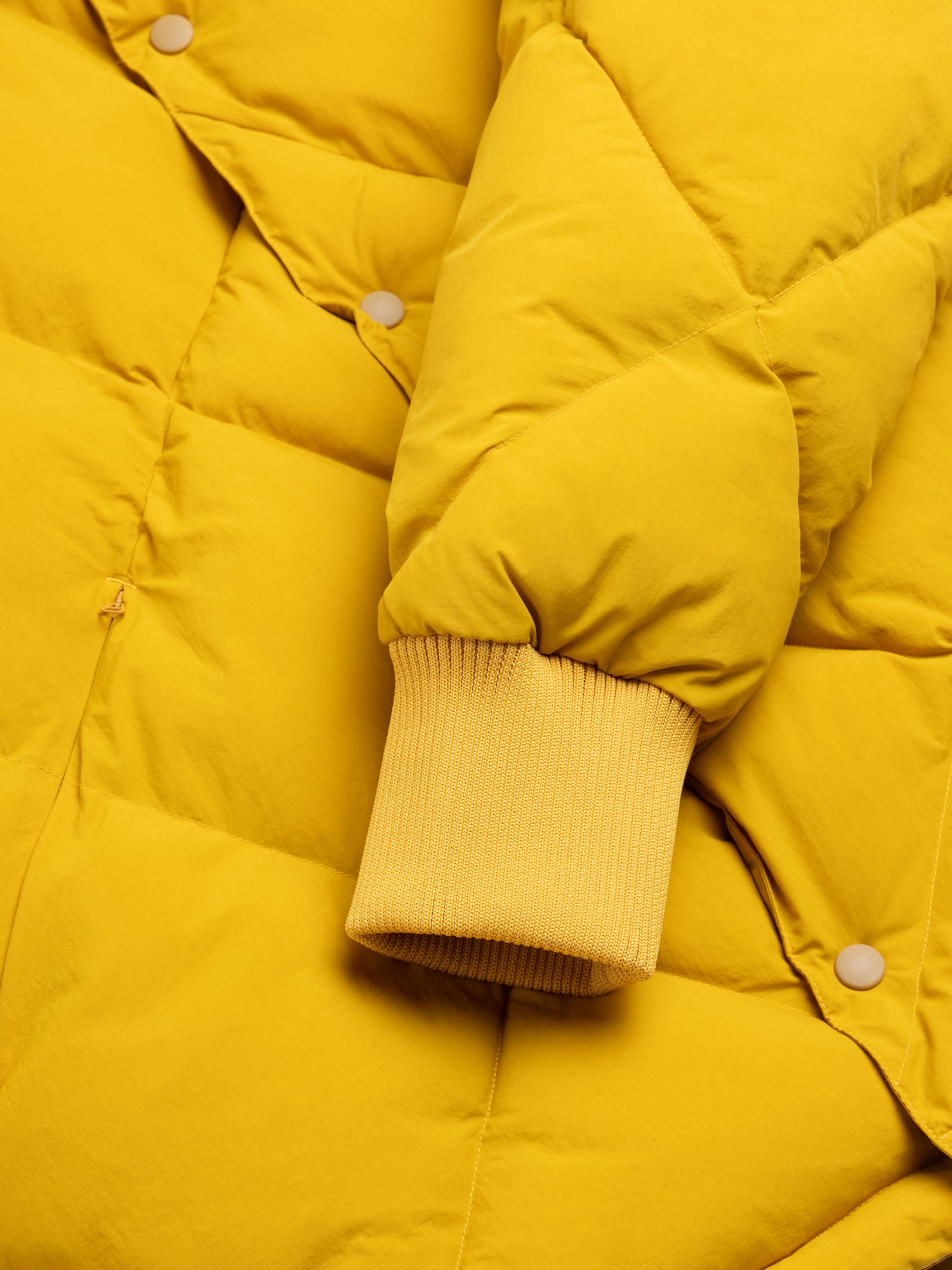 Close-up of a yellow puffer jacket with a focus on the sleeve and button details.