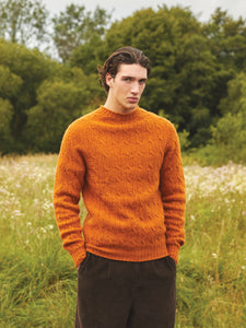 A man wearing the KESTIN Galloway Cable Knit in Tangerine, whilst on the Isle of Skye.