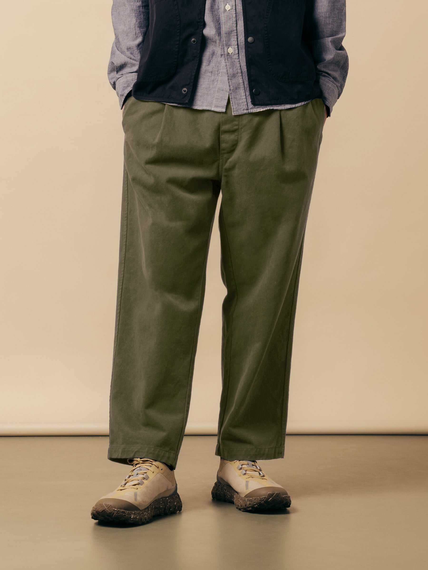 A model wearing olive green trousers with a blue shirt and trail shoes.