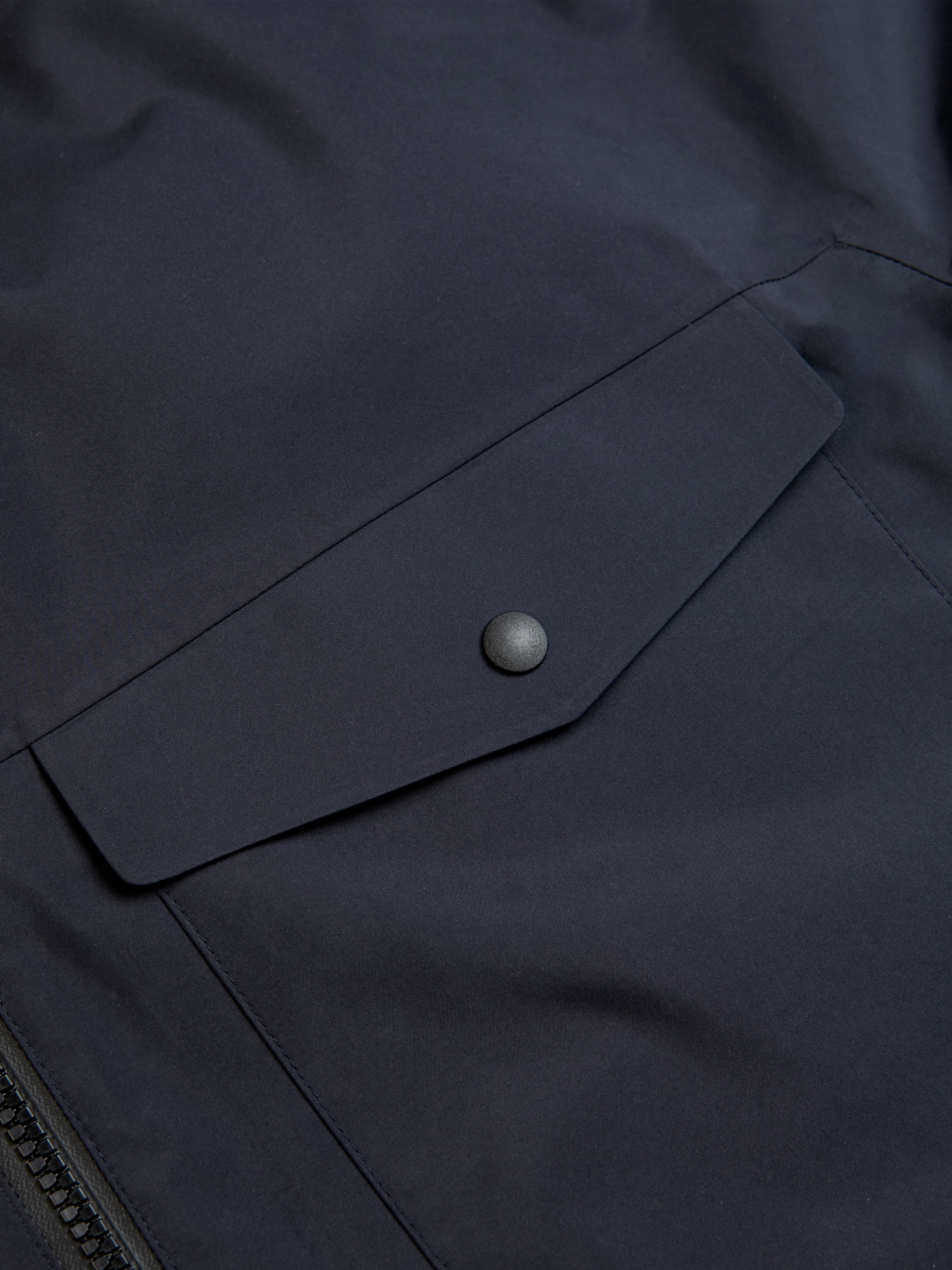 The snap-up patch pocket to the front of a navy blue waterproof shell jacket by KESTIN.
