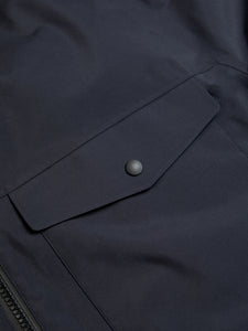 The snap-up patch pocket to the front of a navy blue waterproof shell jacket by KESTIN.