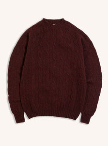 A cable knit sweater in maroon red on a white background, made from Shetland wool.