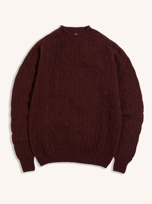 A cable knit sweater in maroon red on a white background, made from Shetland wool.