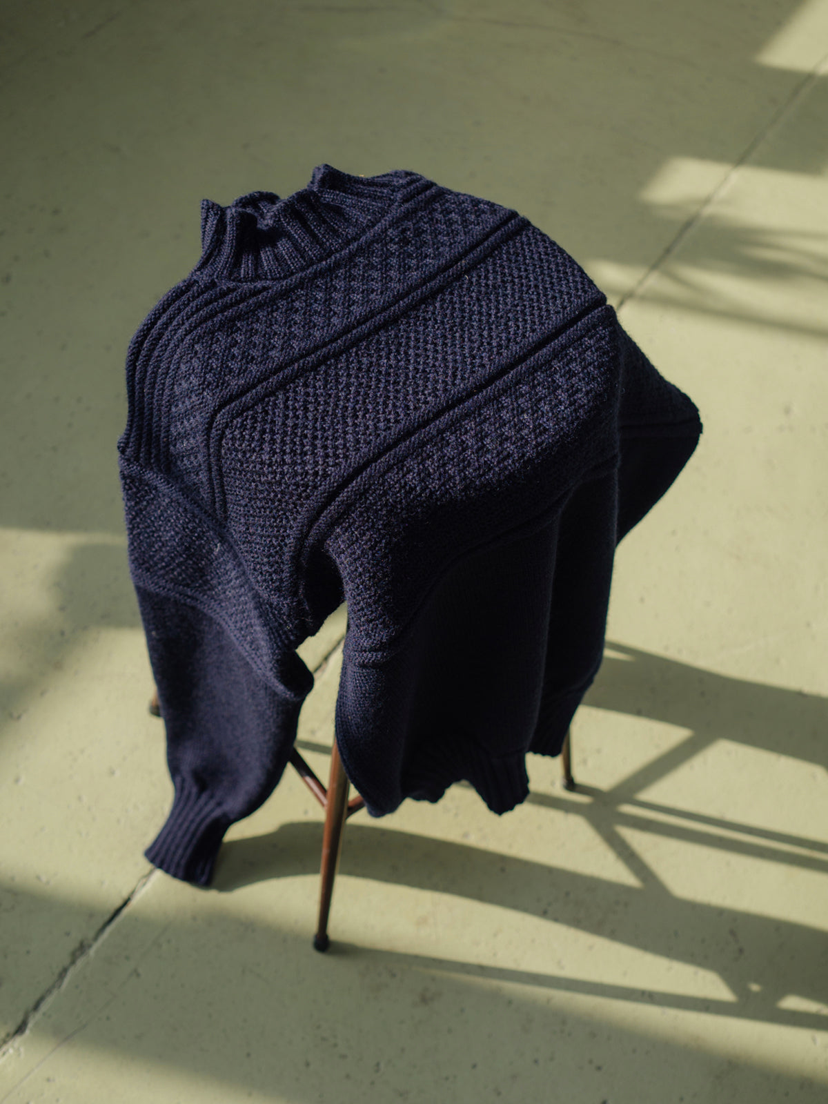 A navy blue merino wool sweater, draped over a wooden stool.