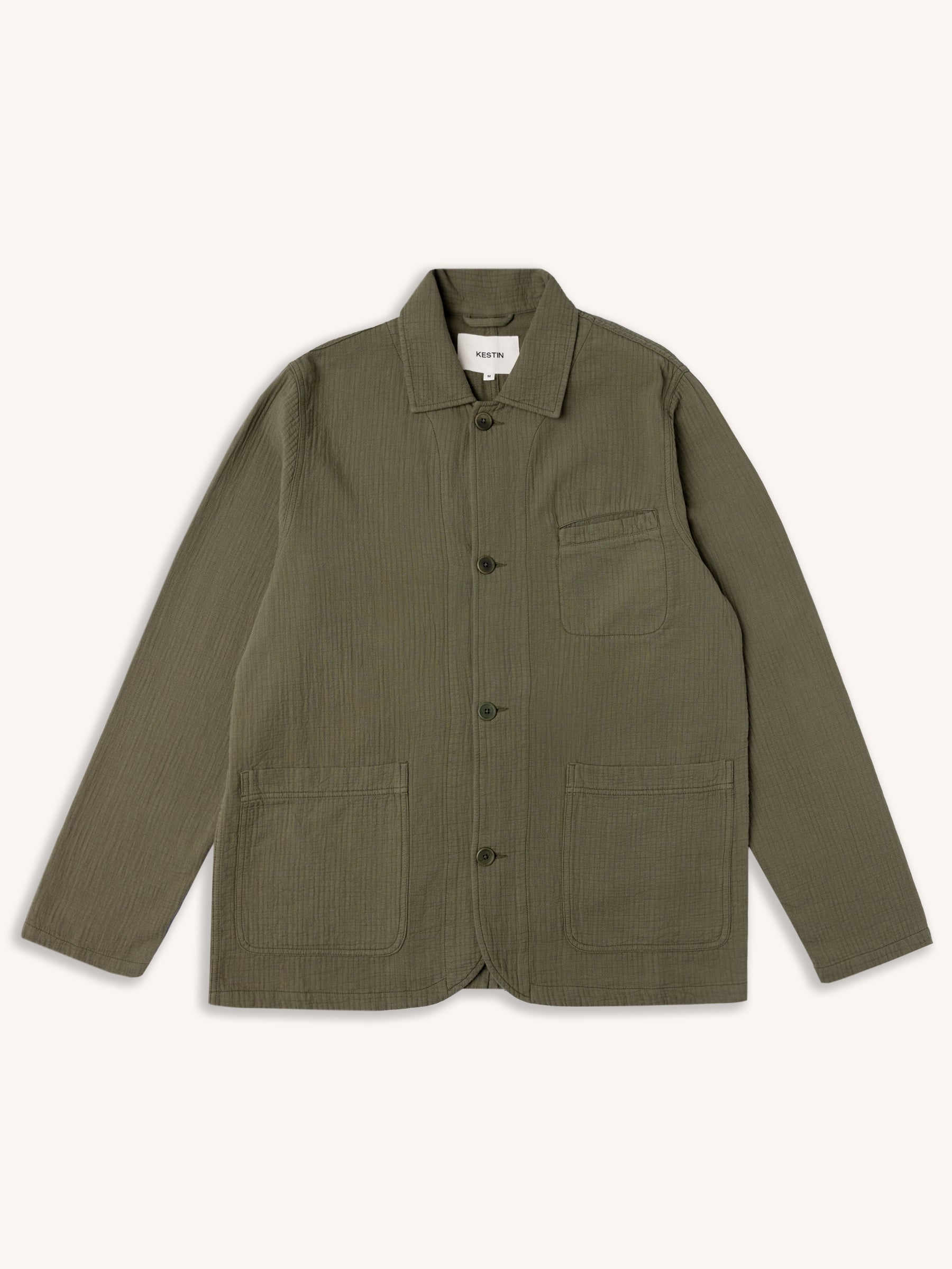 An olive green chore coat-style jacket from menswear brand KESTIN, on a white background.