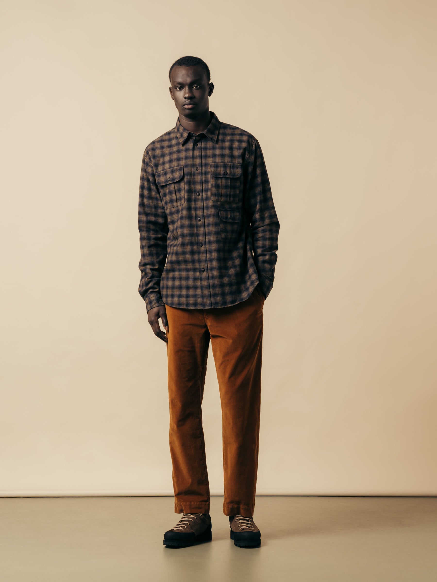 A man wearing a check shirt and brown moleskin trousers from menswear brand KESTIN.