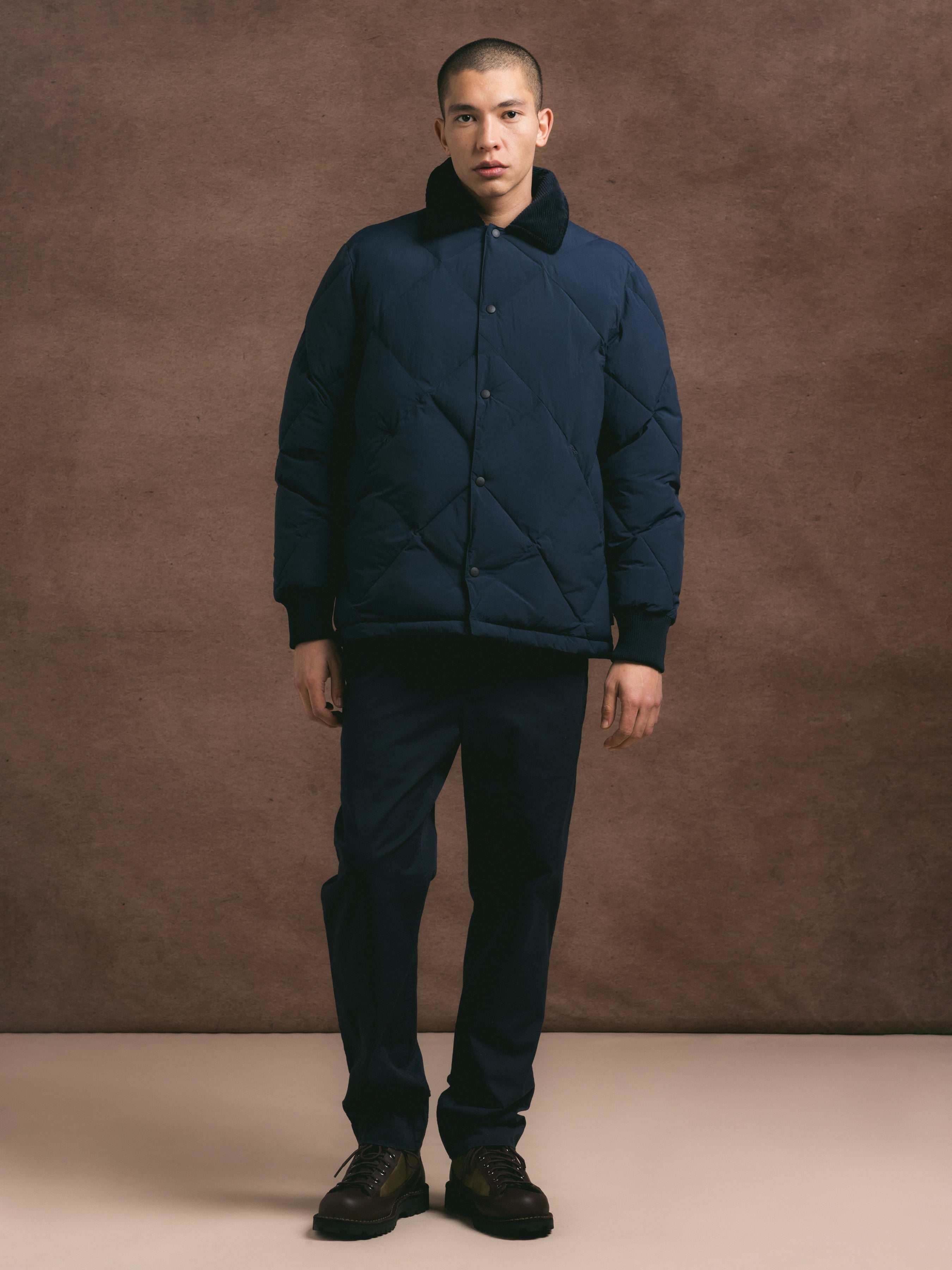Man wearing a dark blue quilted jacket against a brown background