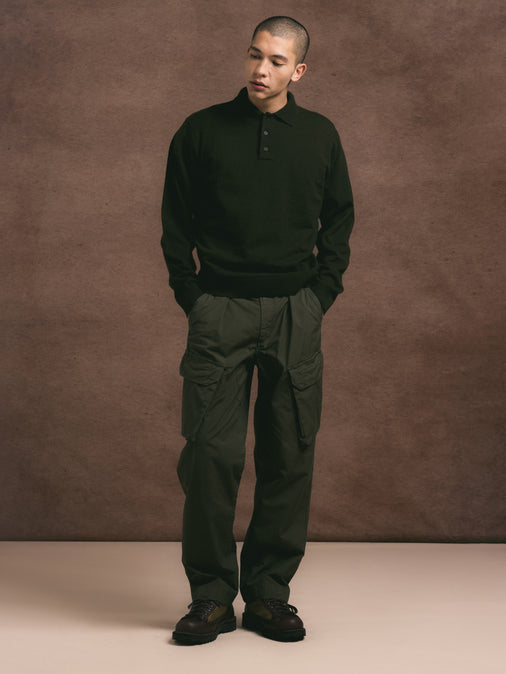 Man wearing a dark green sweater and pants against a brown background