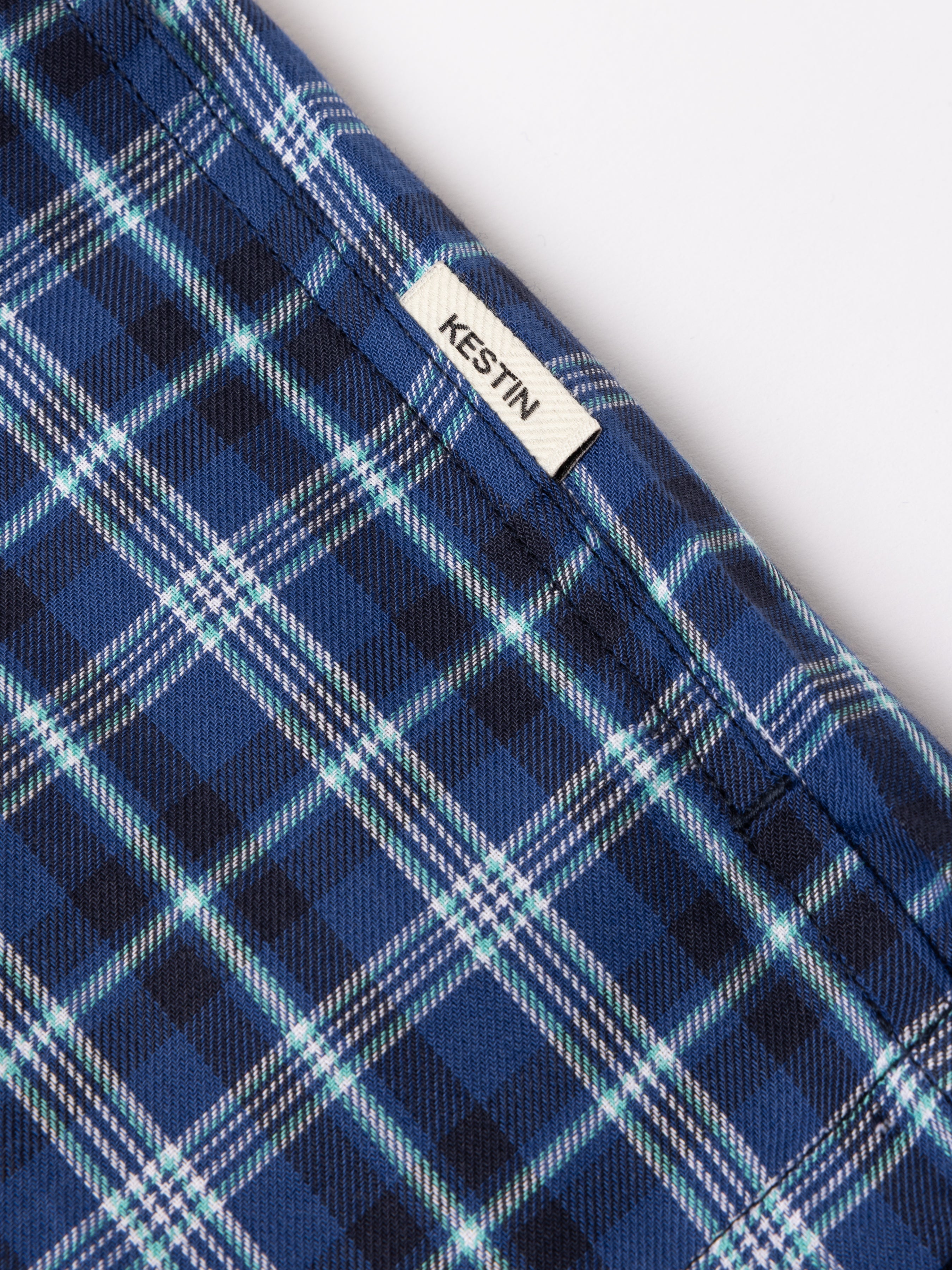 Close-up of blue plaid fabric with 'Kestin' label on a white background