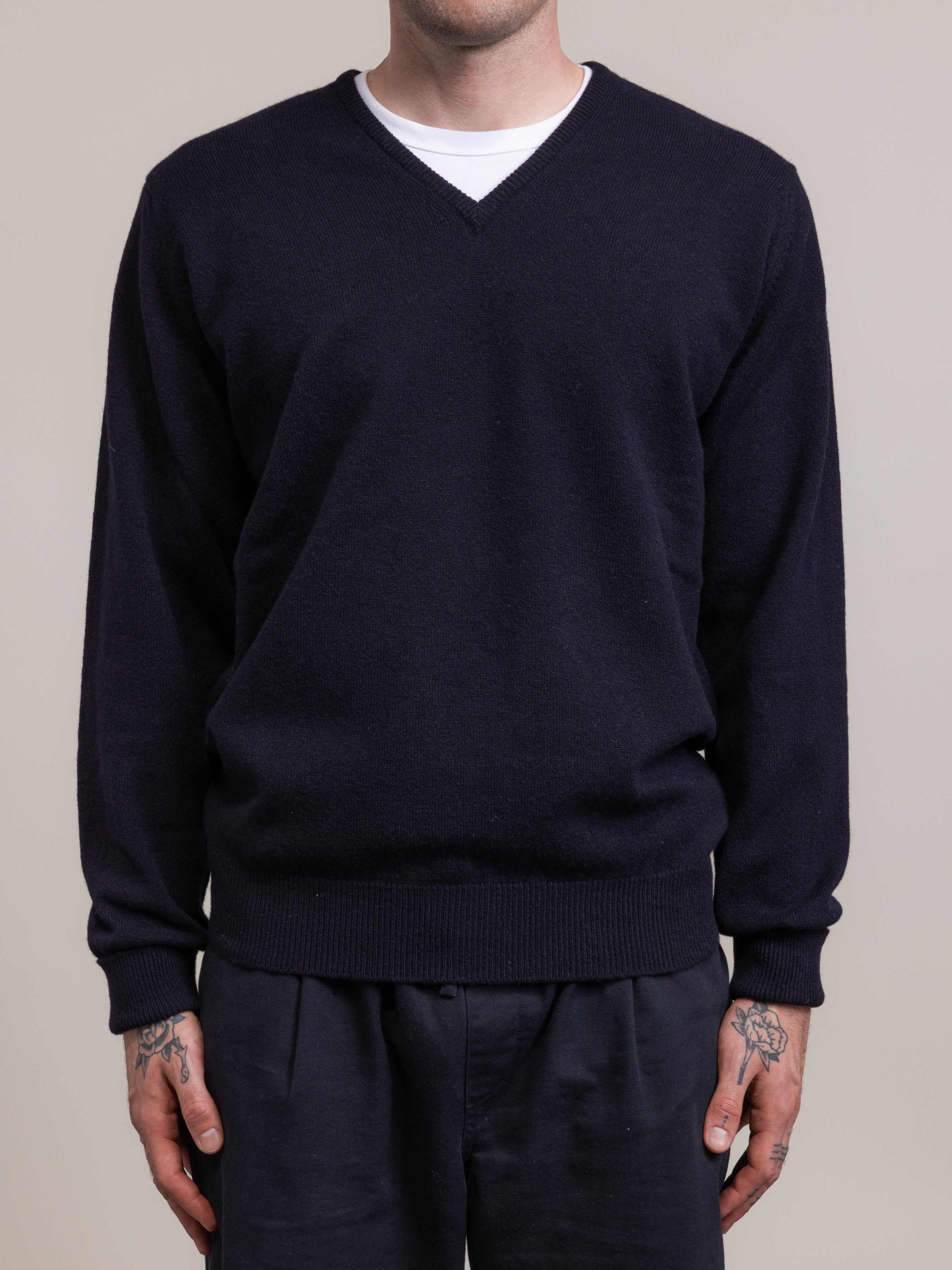 Person wearing a dark blue v-neck sweater over a white t-shirt on a plain background