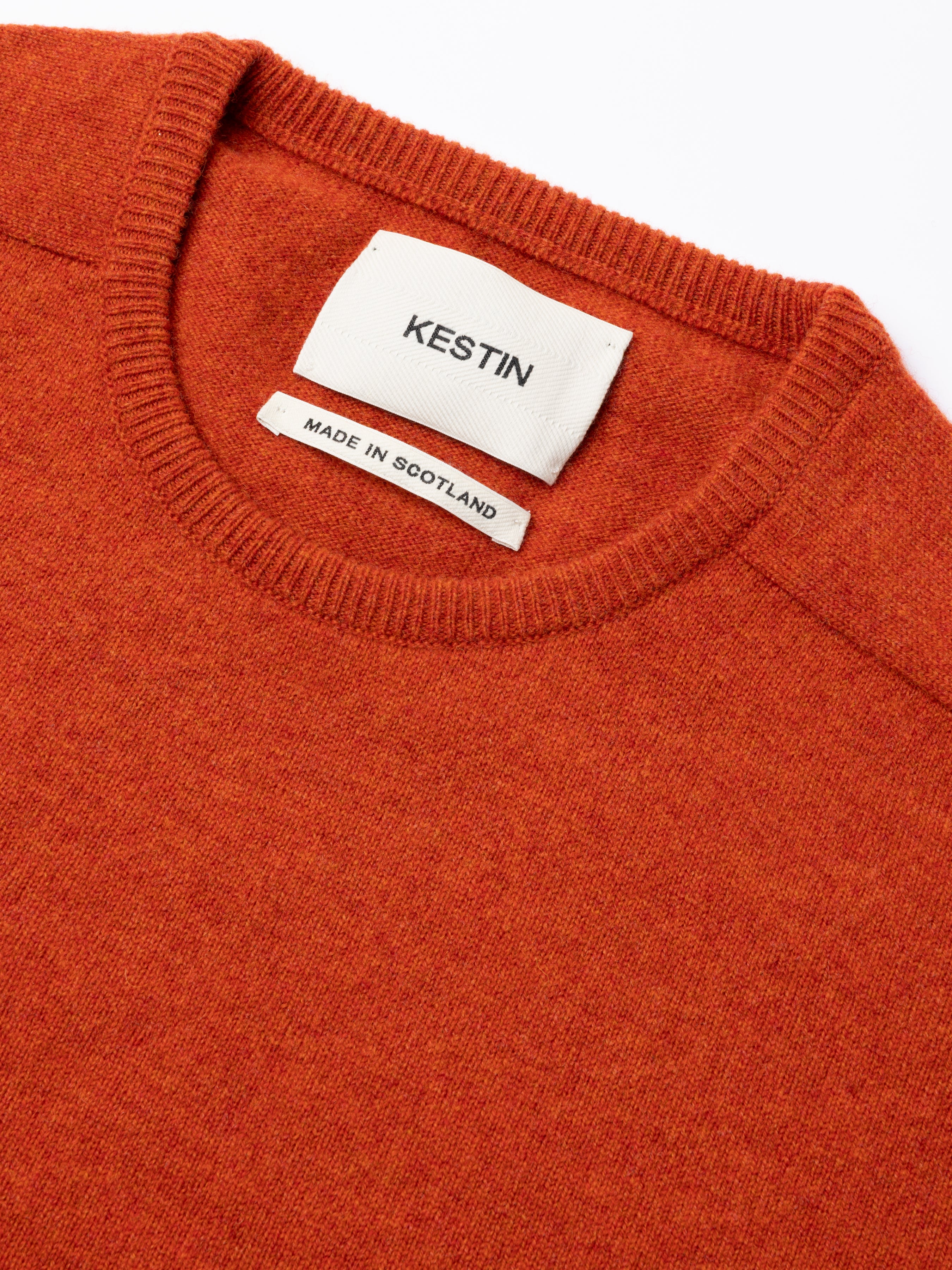 Close-up of an orange sweater with a Kestin label on a white background
