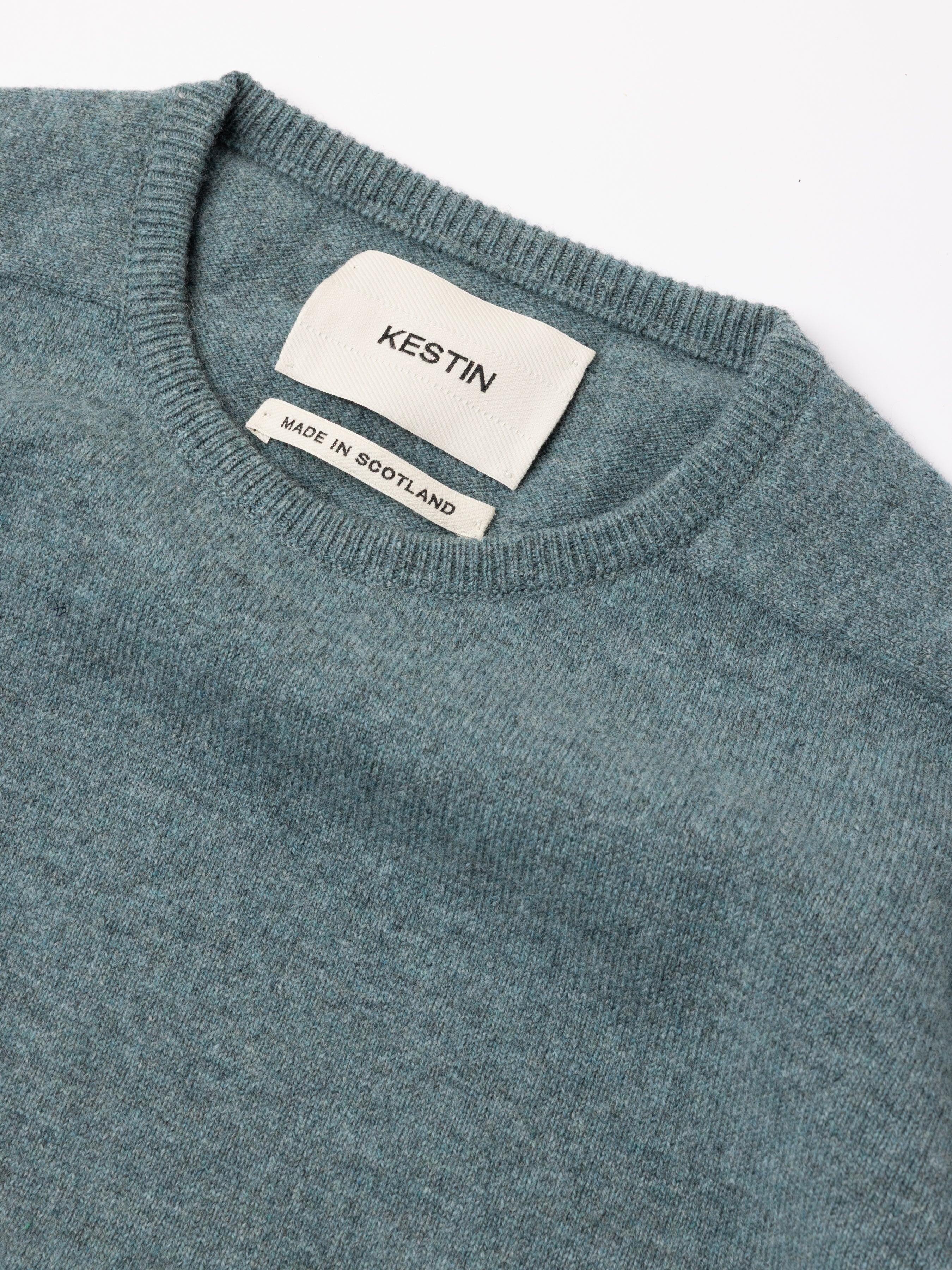 Close-up of a teal sweater with a Kestin label on a white background
