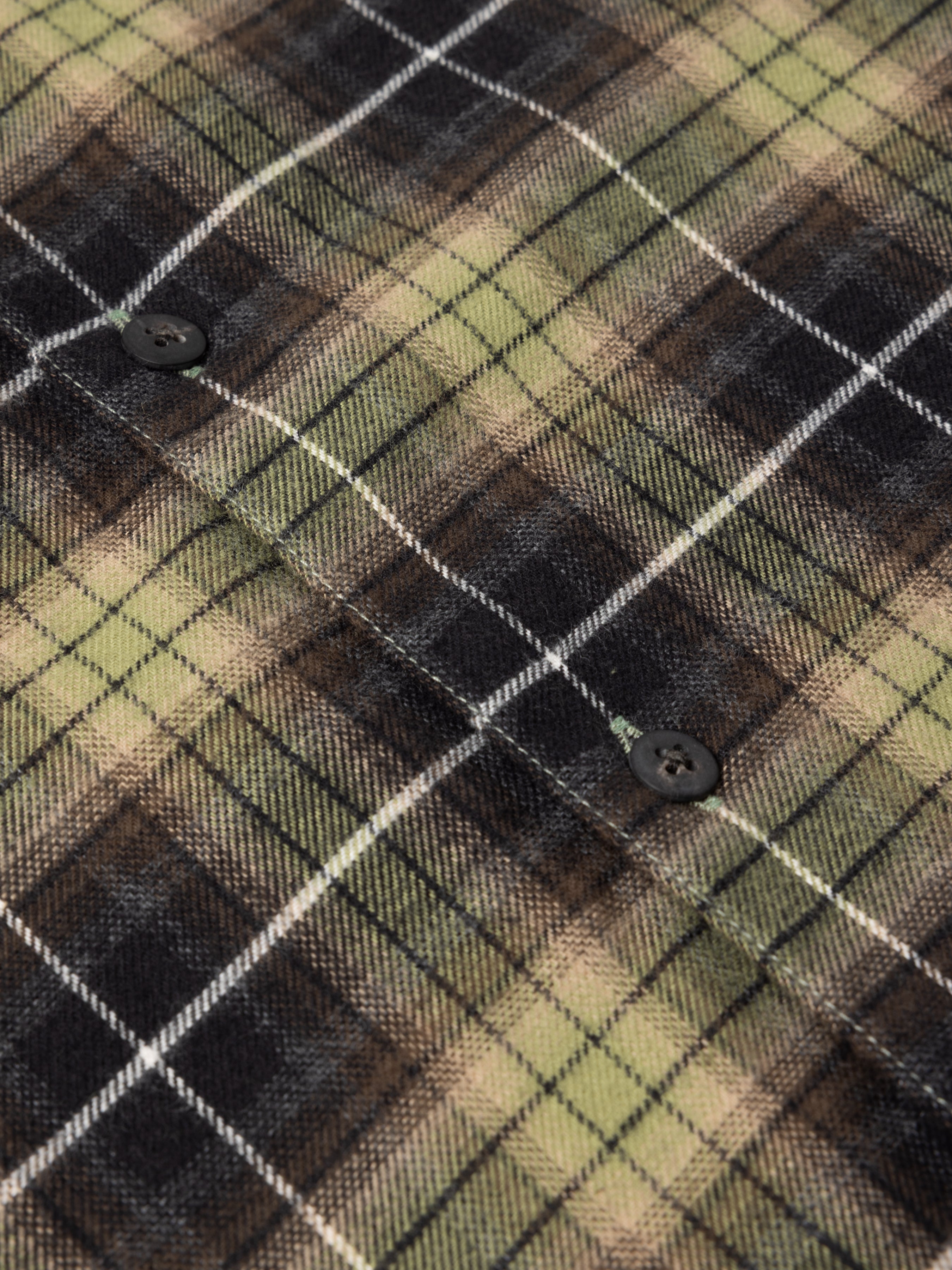 Close-up of a plaid fabric with green, brown, and black colors.