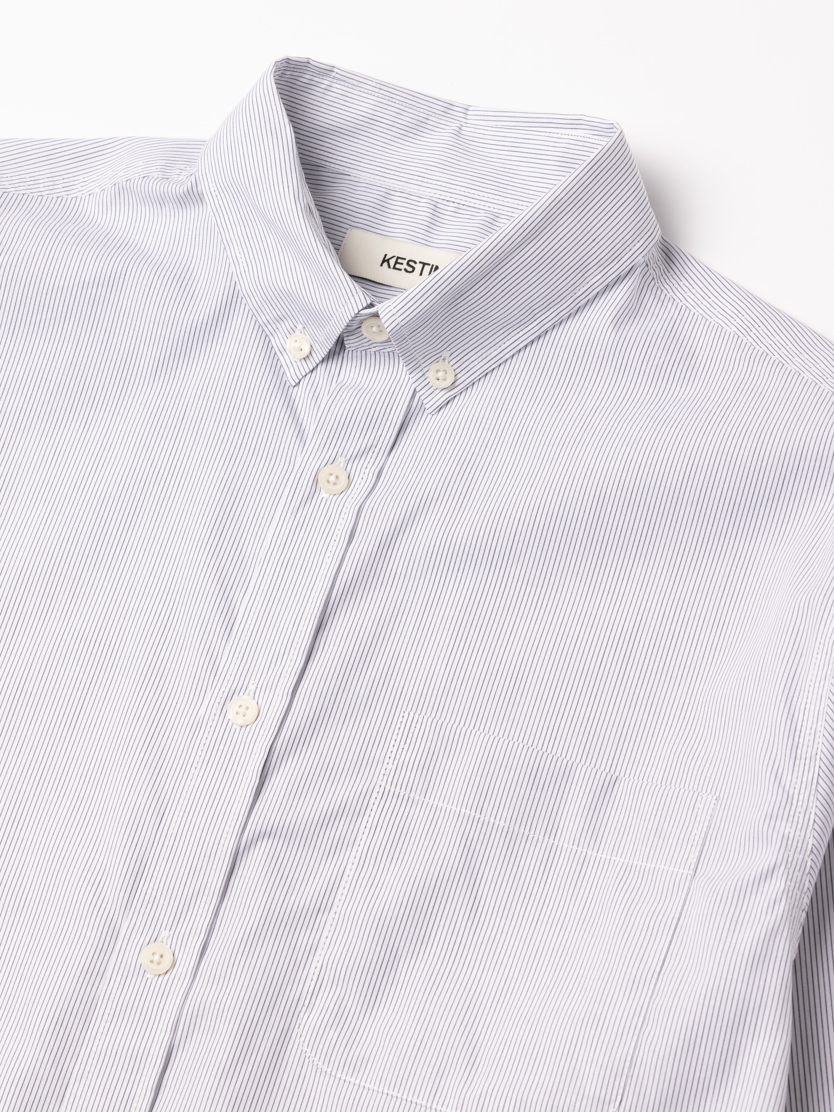 Close-up of a light blue striped shirt with a collar, featuring a KESTIN label