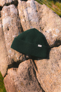 A dark green knitted wool beanie, sitting on a rock.