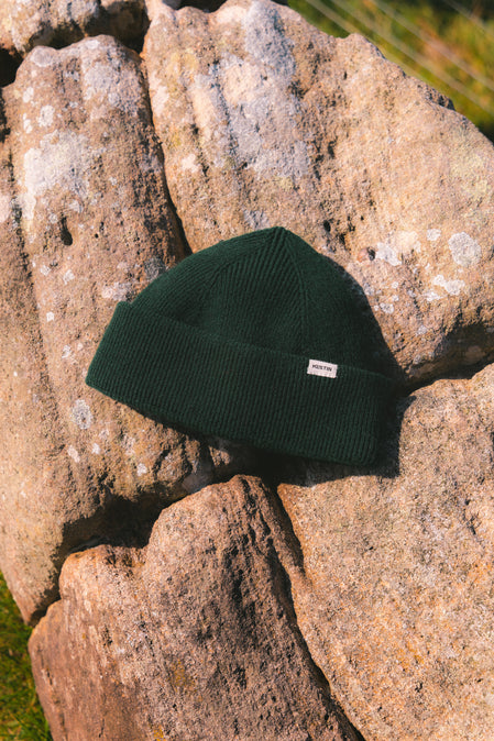 A dark green knitted wool beanie, sitting on a rock.